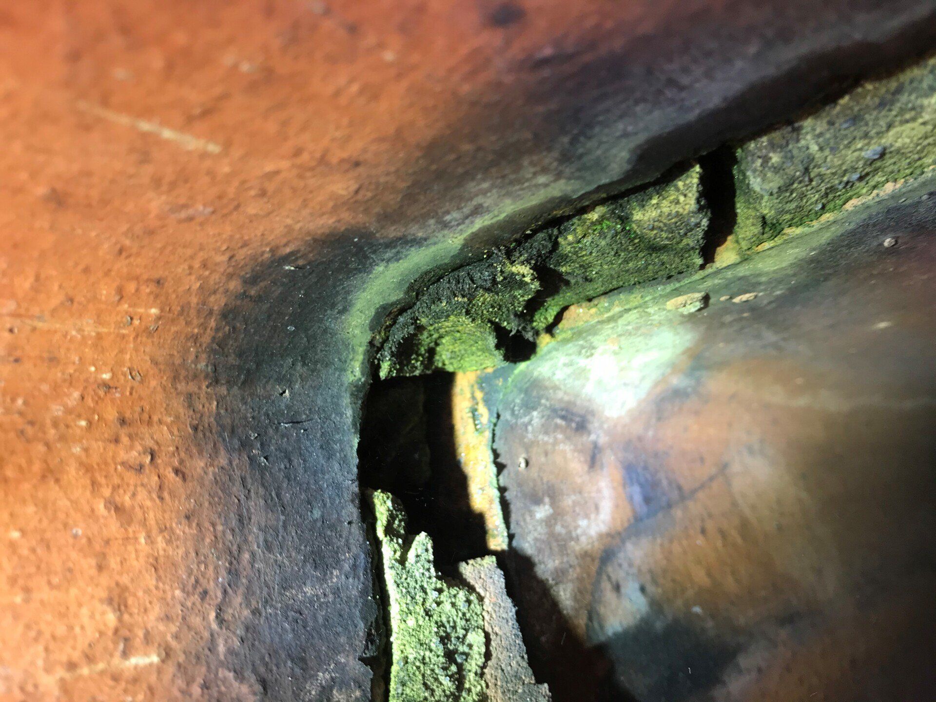 Close-up view inside a chimney flue, showing damaged, cracked brickwork with green moss and dark staining.