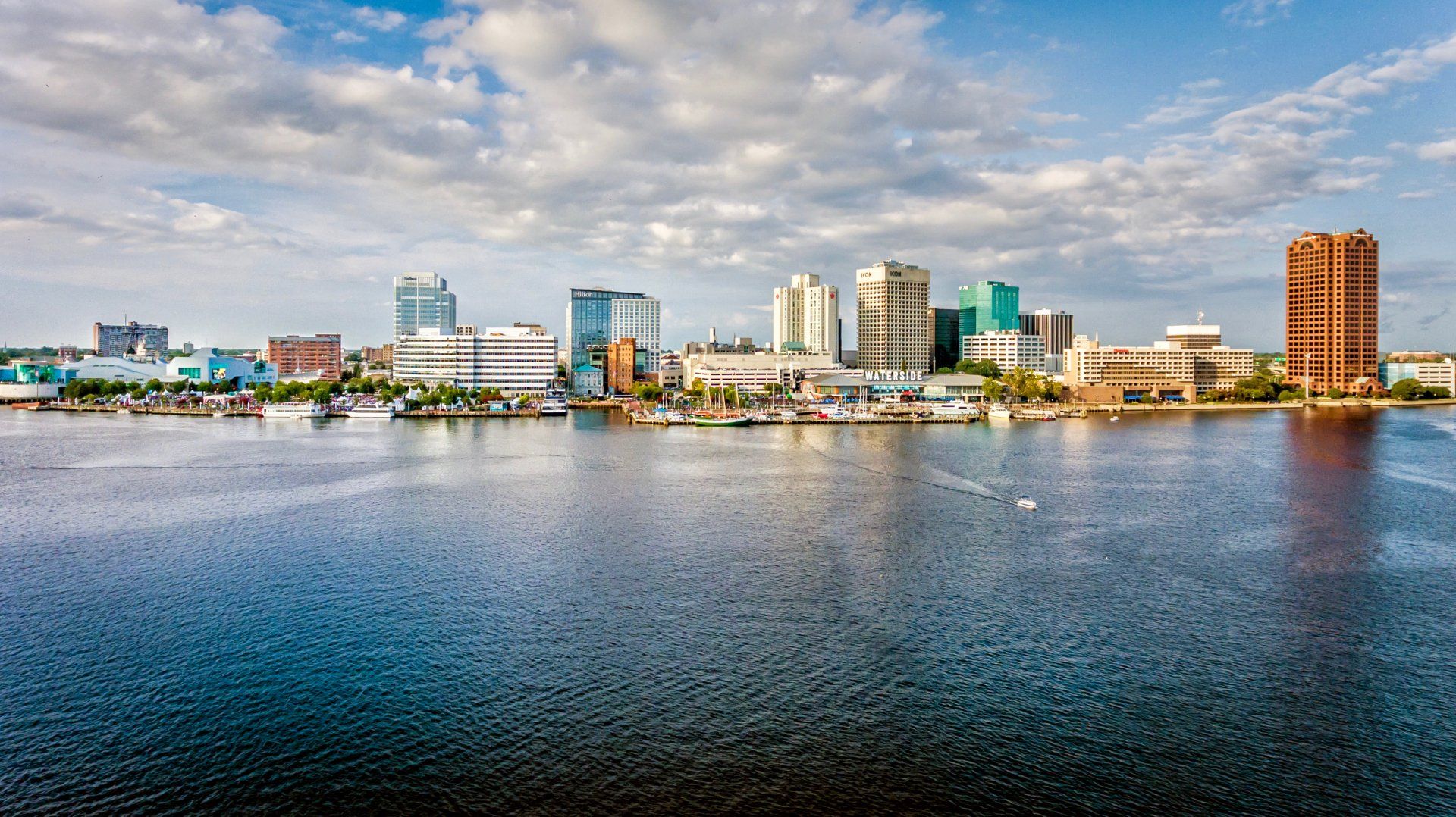 Skyline of Norfolk, Virginia, seen from across the water. Various buildings and a brick tower are visible under a cloudy sky.