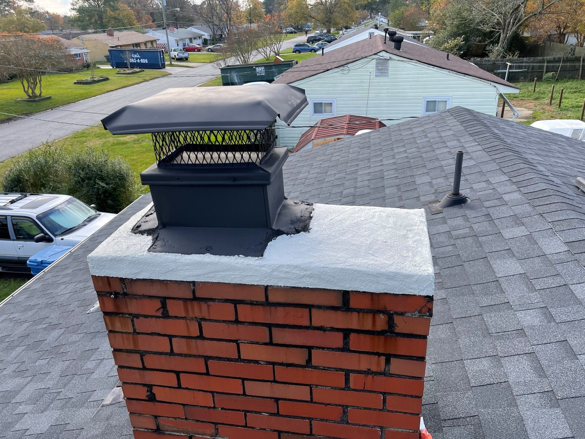 Brick chimney with a dark chimney cap, on a roof with gray shingles.