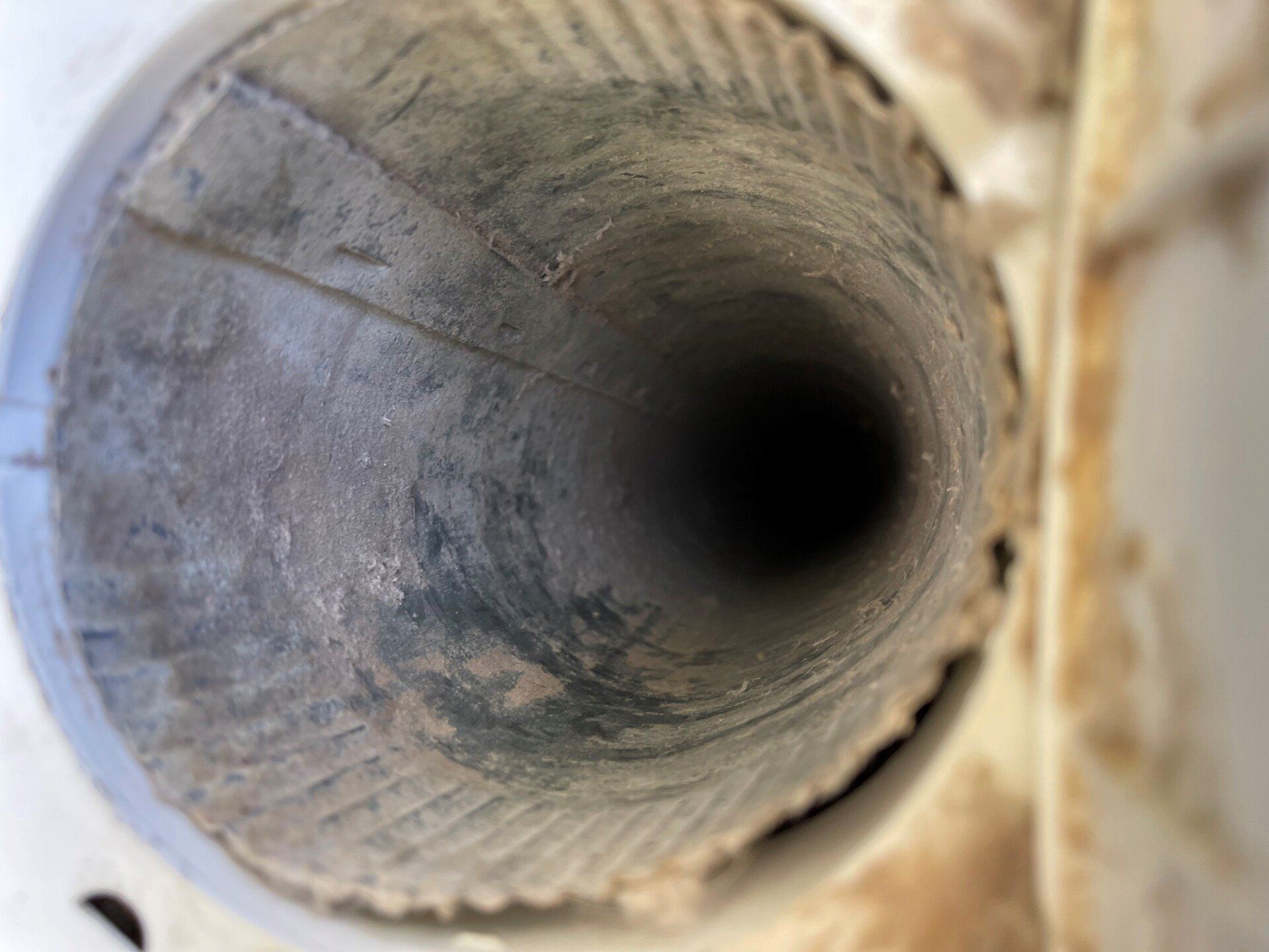 Looking down a dirty, circular vent with textured walls and a dark interior.