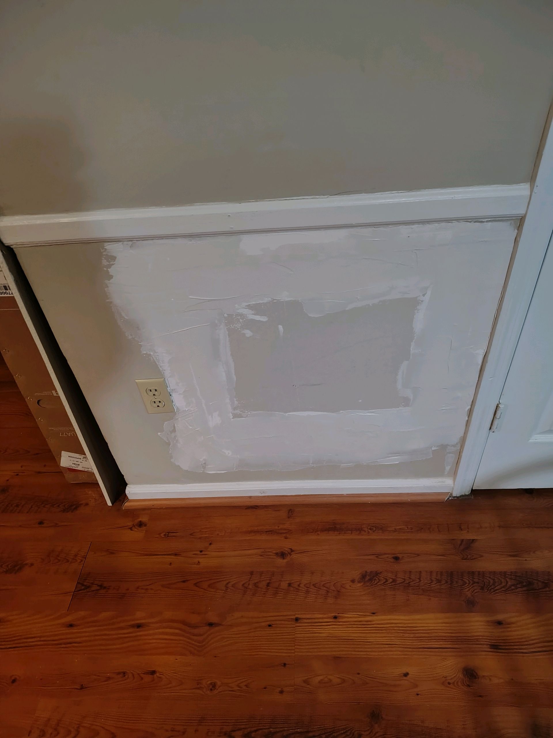 White wall panel with patchwork repair above hardwood floor in a room corner