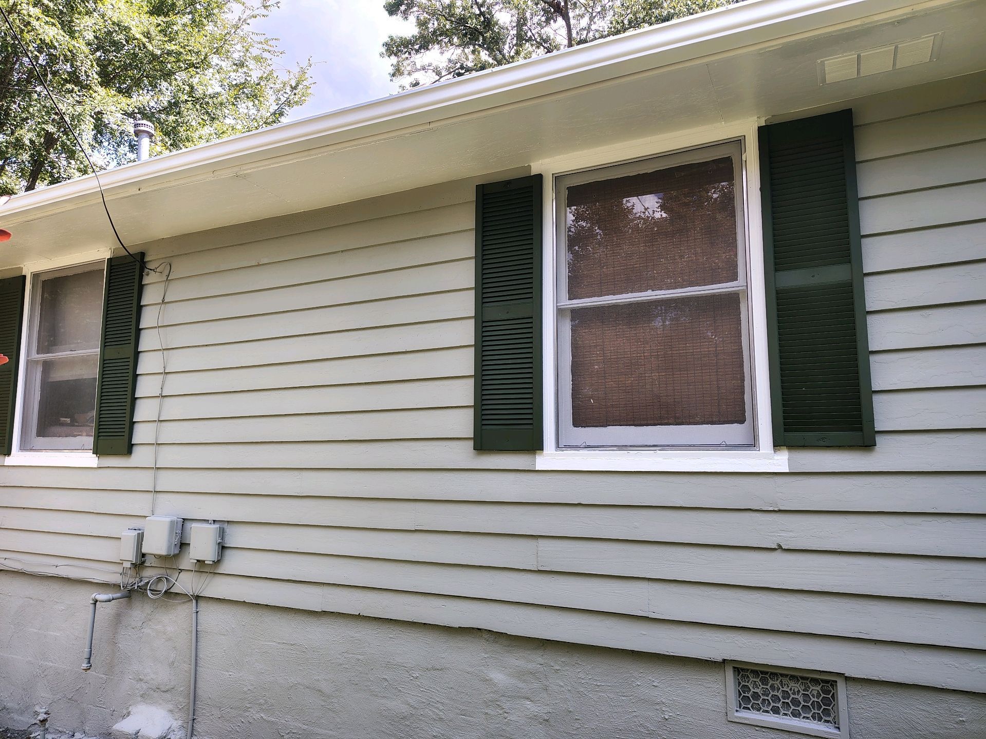 Exterior of a light gray house with white-trimmed windows and dark green shutters