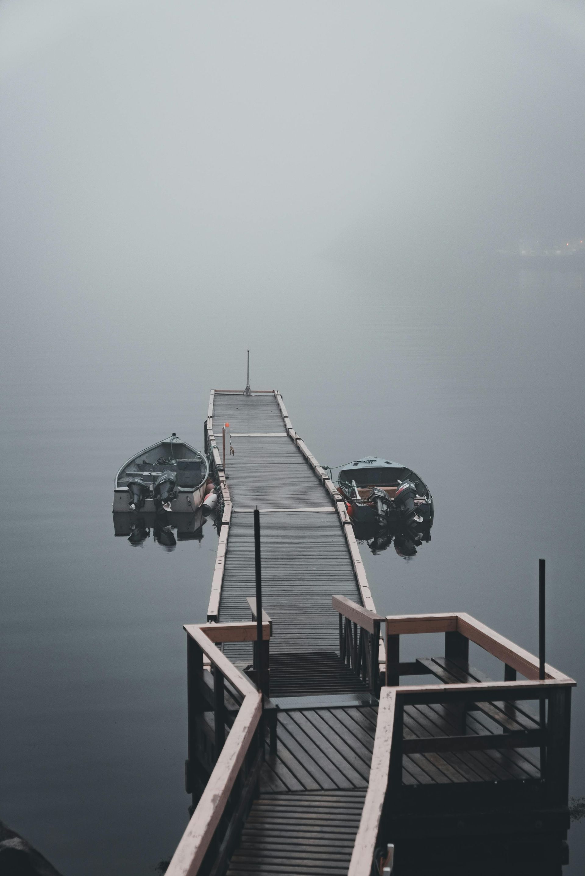 Foggy dock extending into calm water with two small boats moored on either side