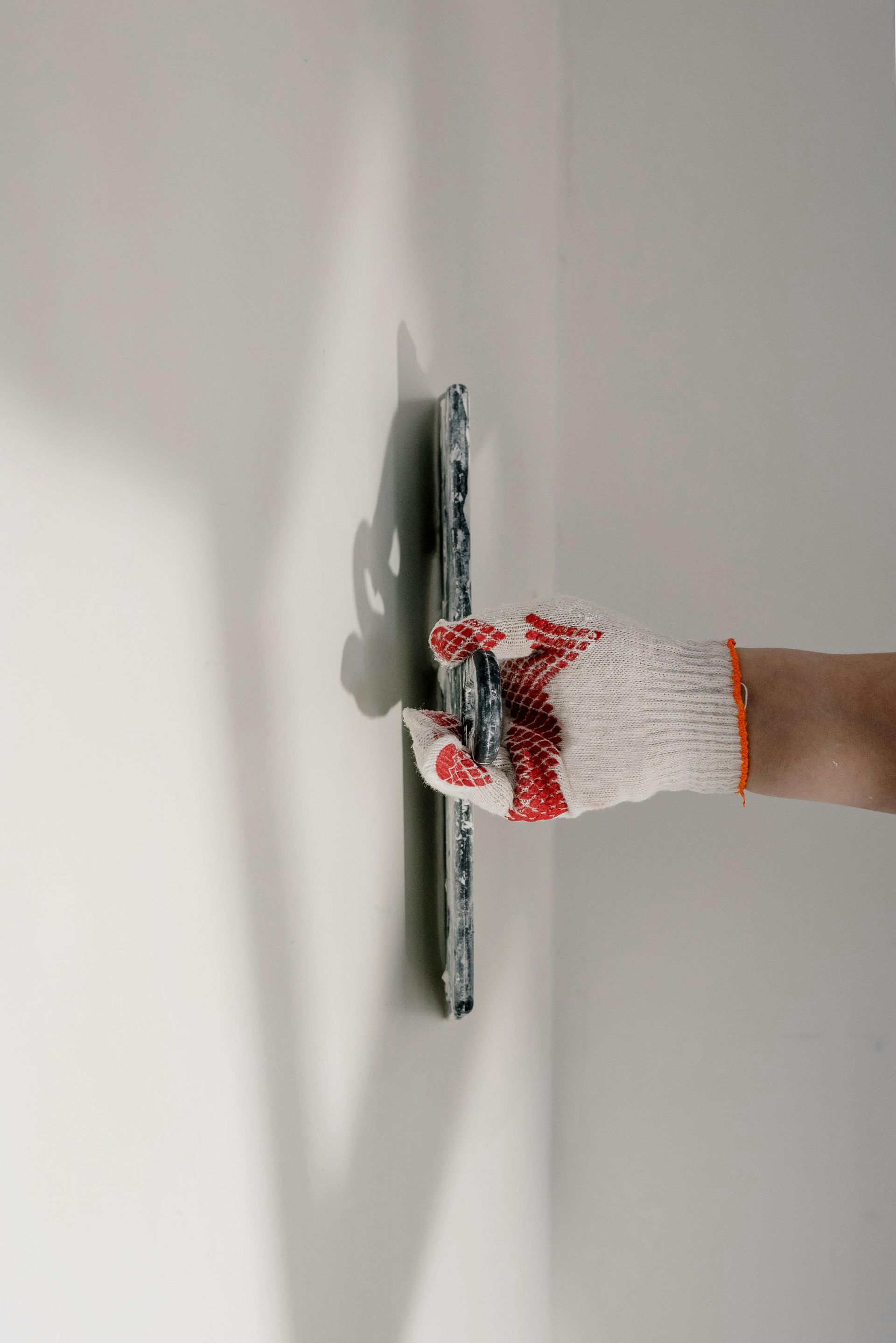 Gloved hand using a wall sander on a white wall, with dust around the tool