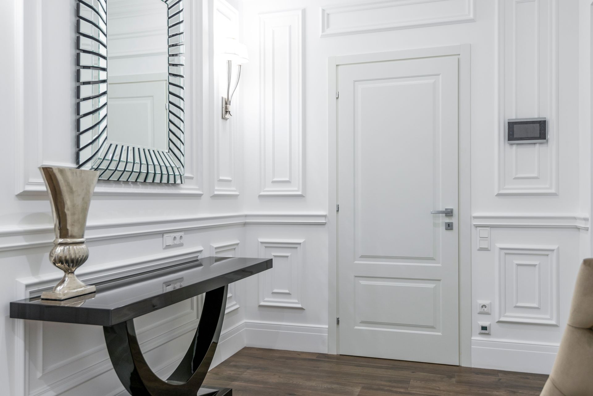 Elegant white hallway with paneled walls, decorative mirror, console table, and dark wood floor
