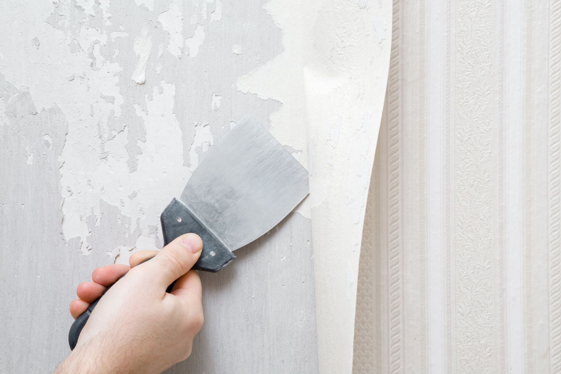Hand scraping old white paint from a wall with a putty knife