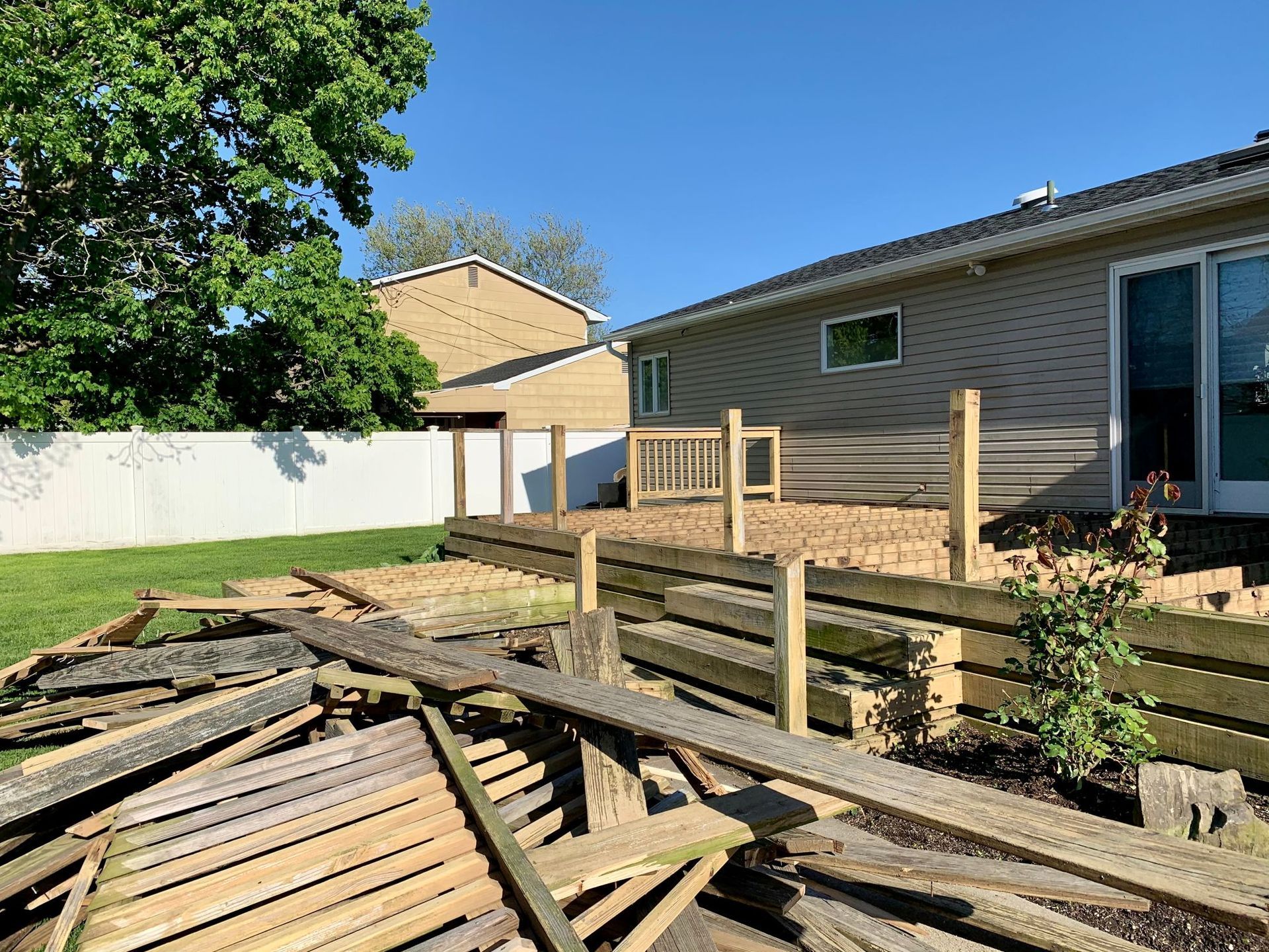 Backyard with a raised wooden deck under construction beside a house, with lumber and tools scattered below