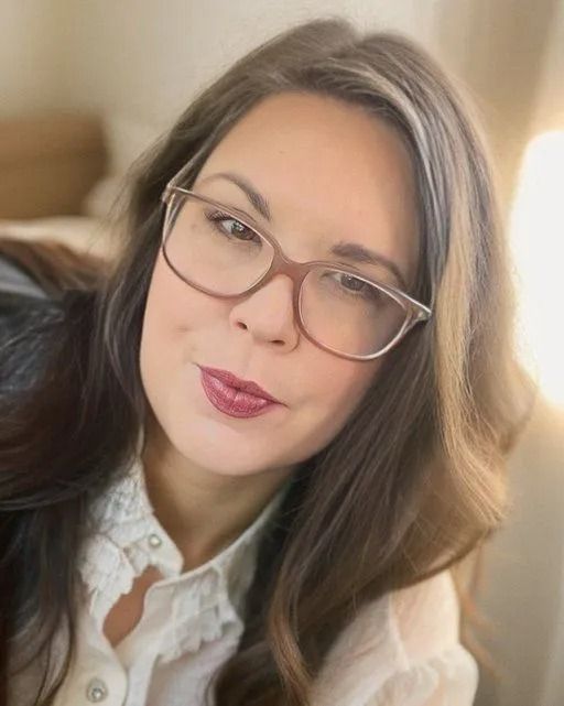 A woman wearing glasses and a white shirt is smiling for the camera.