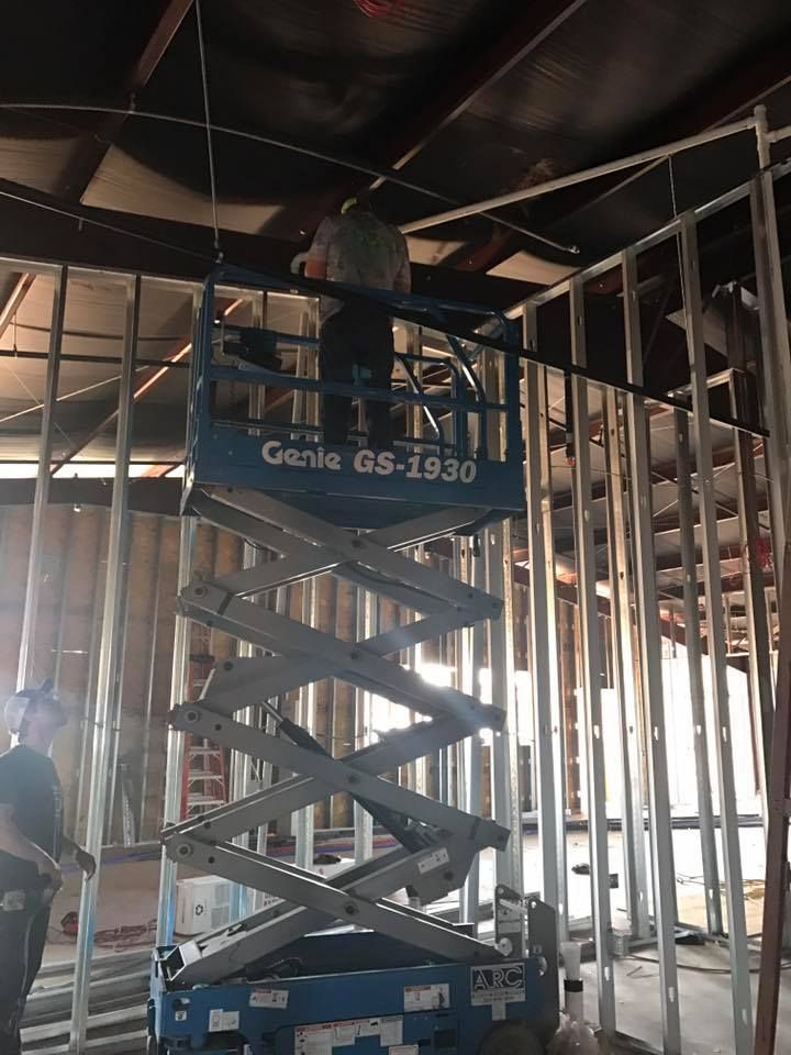 A man is standing on a genie scissor lift in a building under construction.