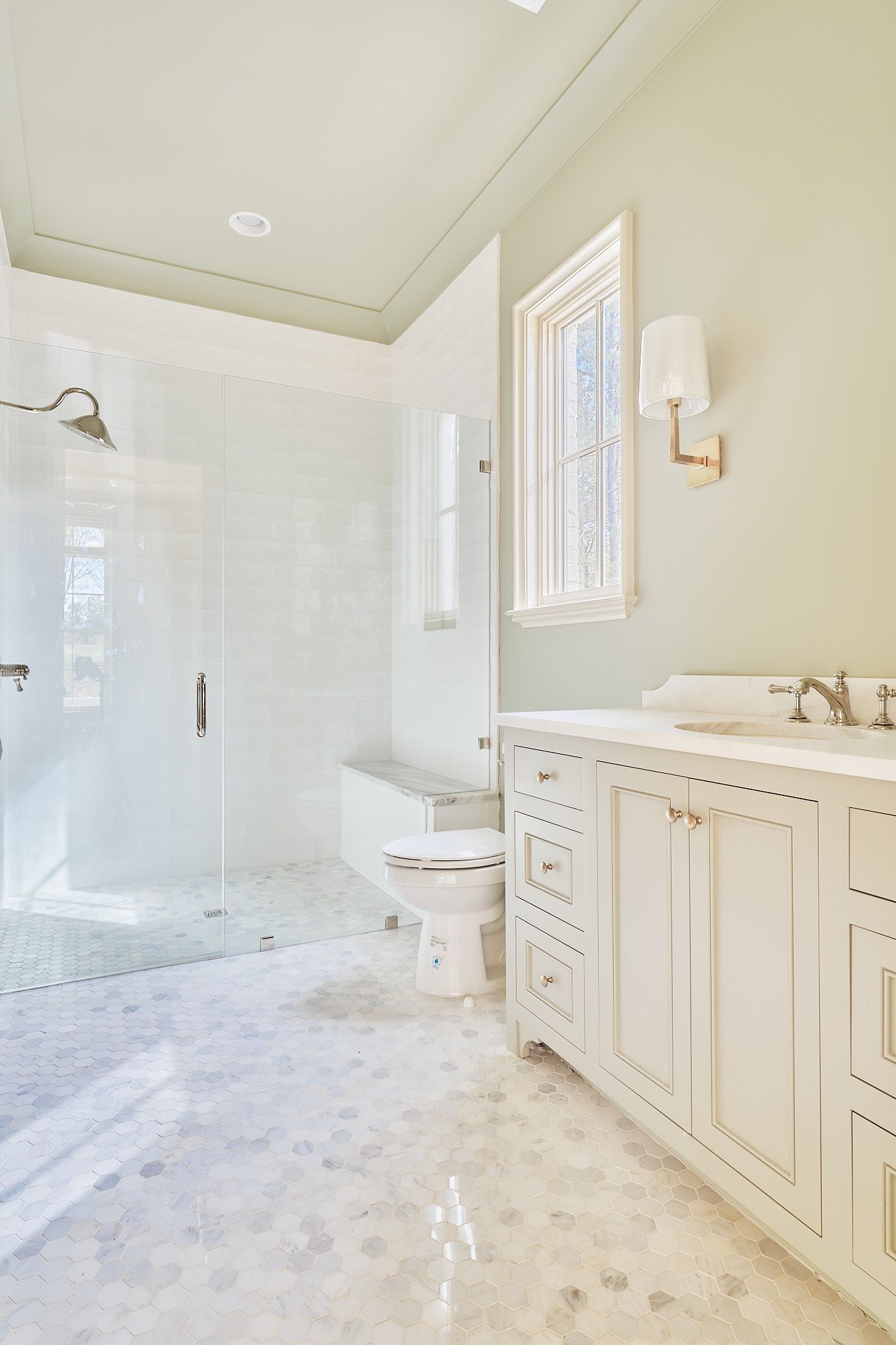 Bright white bathroom with glass shower, toilet, vanity, and window blinds