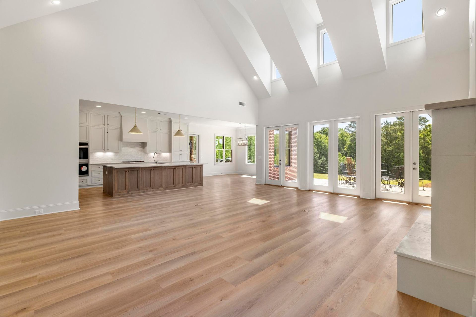 Bright open living room with wood floors, vaulted ceiling, and large windows overlooking greenery