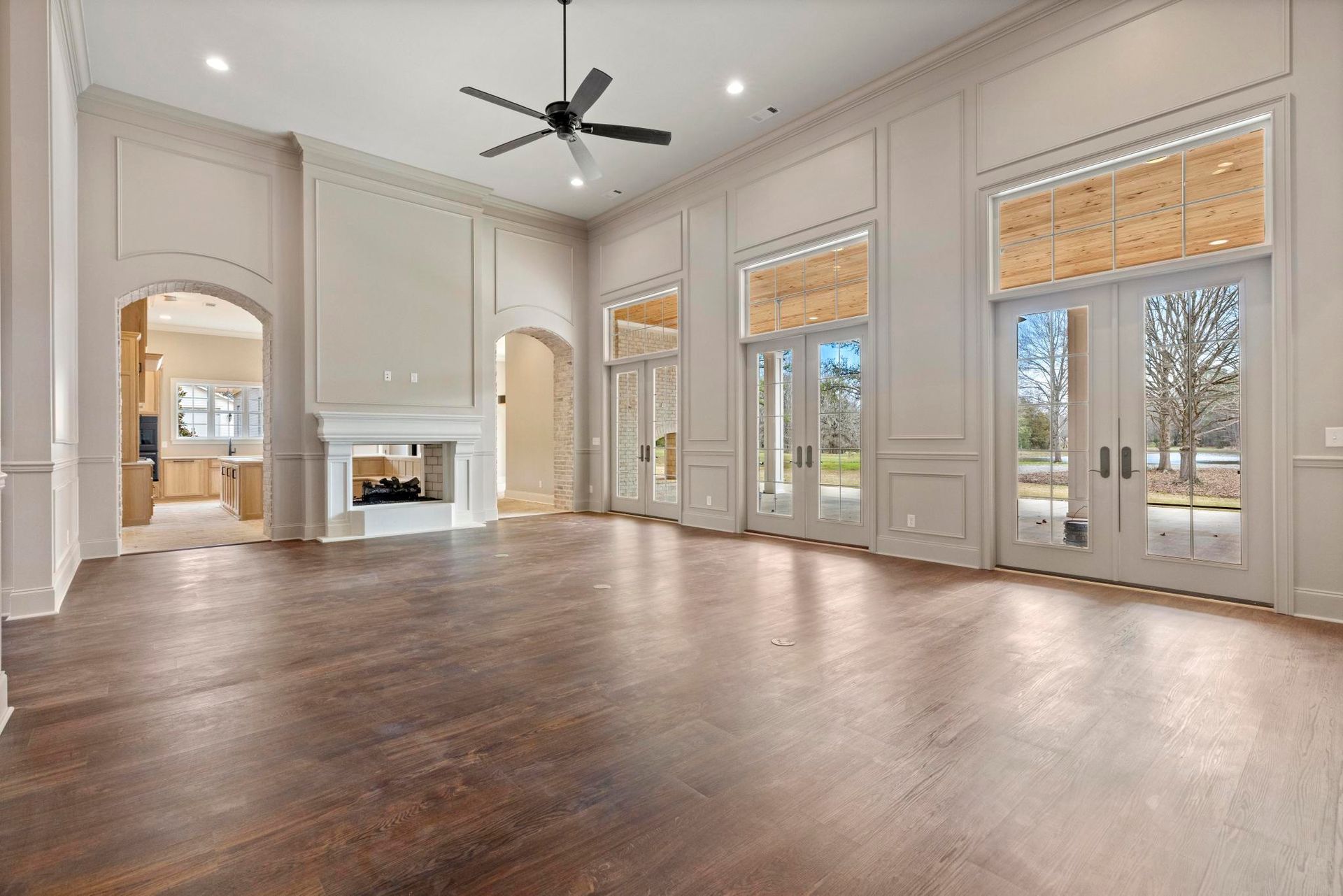 Bright empty living room with hardwood floors, vaulted ceiling, fireplace, and large windows with blinds