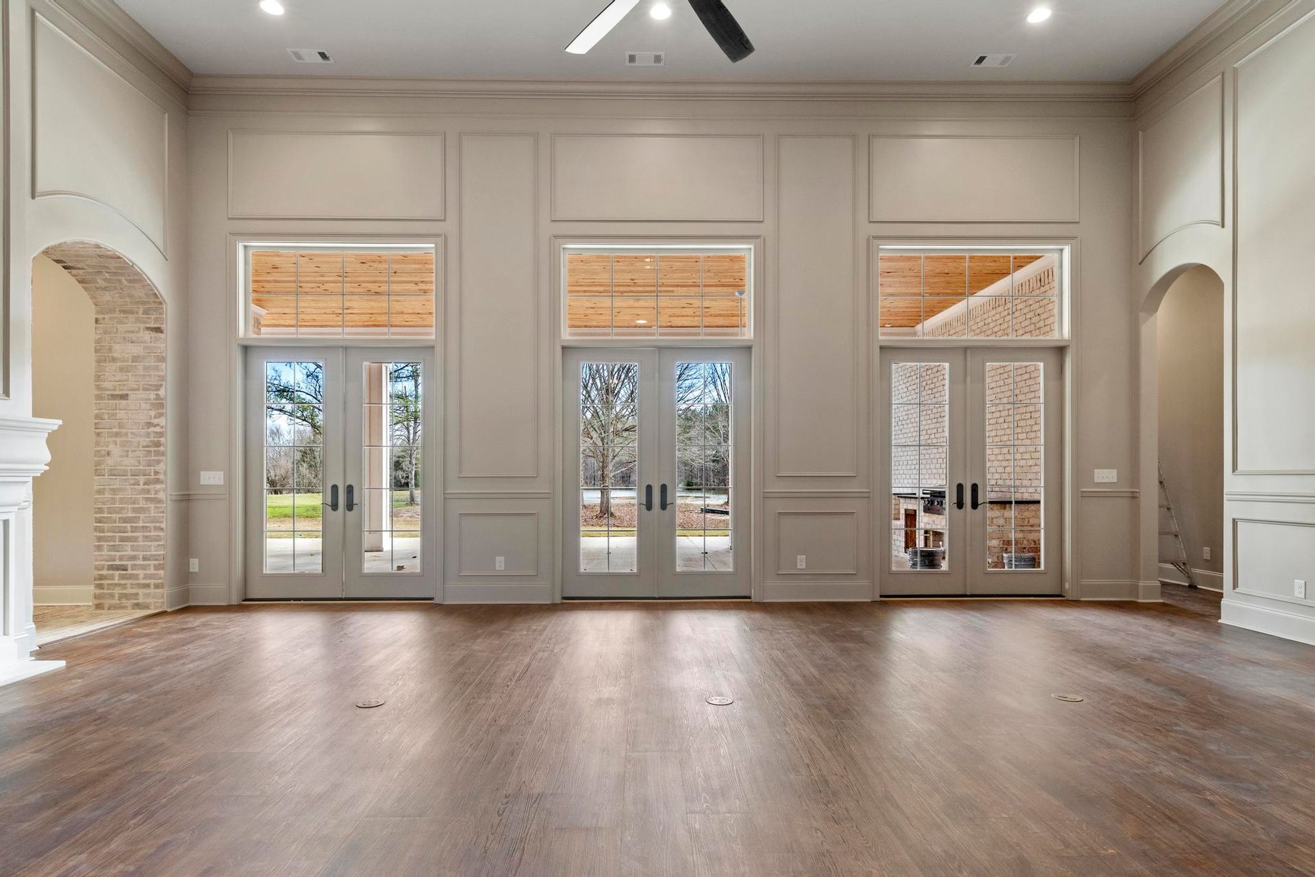 Spacious empty room with hardwood floors, tall windows, white walls, and ceiling fans