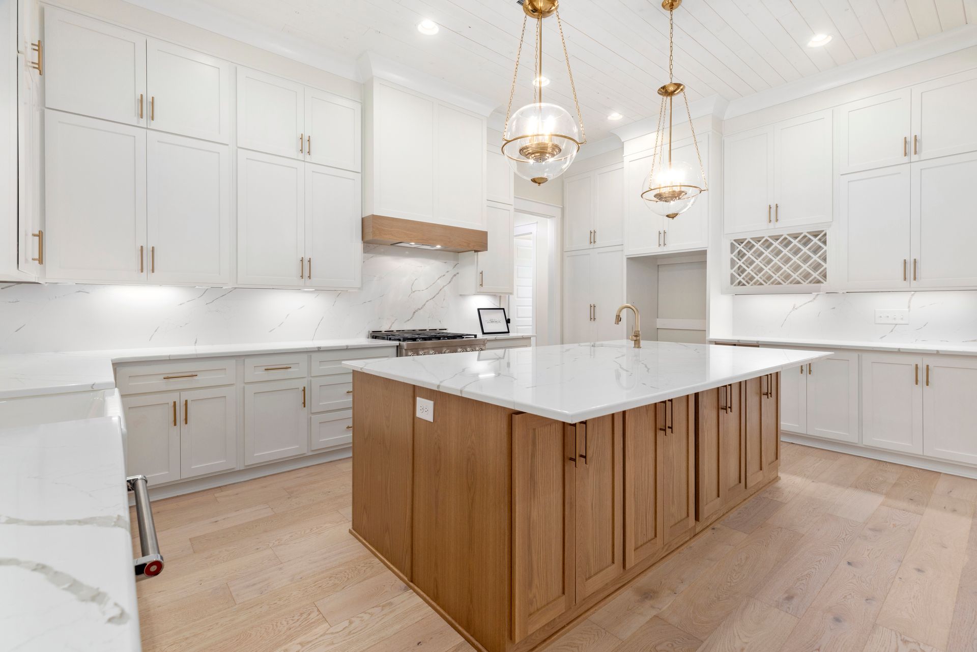 Bright modern kitchen with white cabinets, marble island, and wood base accents