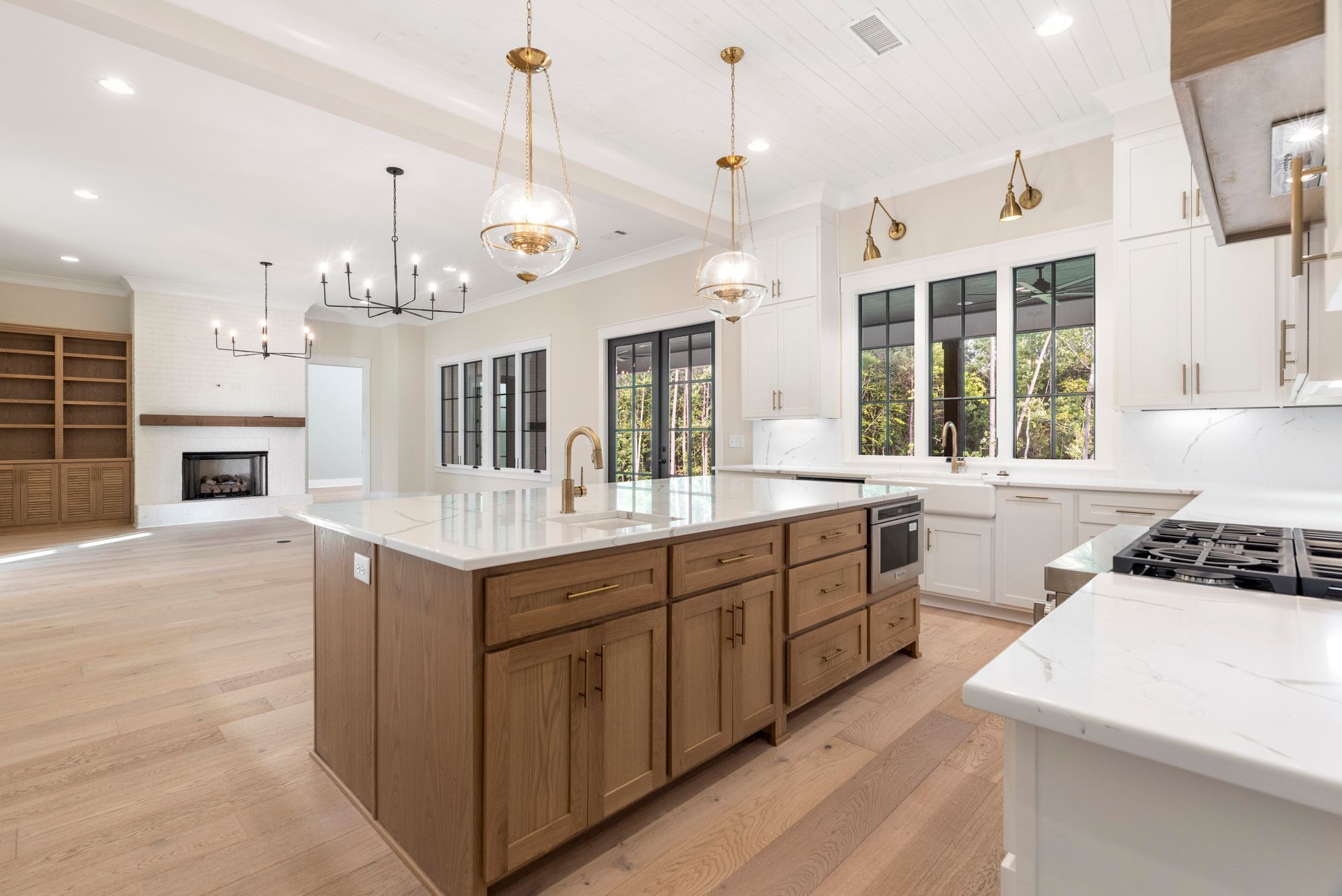 Bright modern kitchen with white cabinets, large island, gold pendant lights, and wood flooring