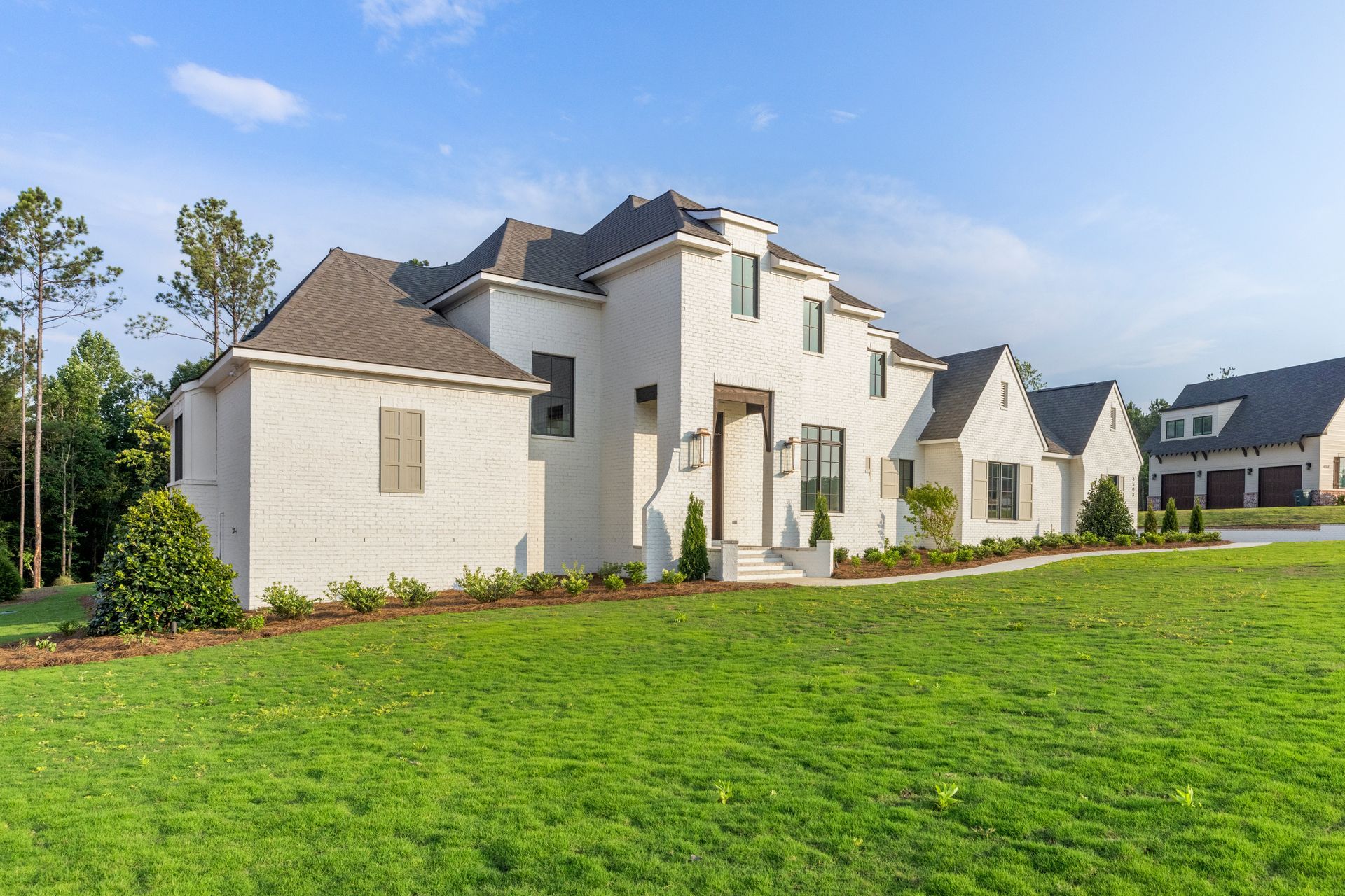 Large white suburban house with a green lawn and blue sky
