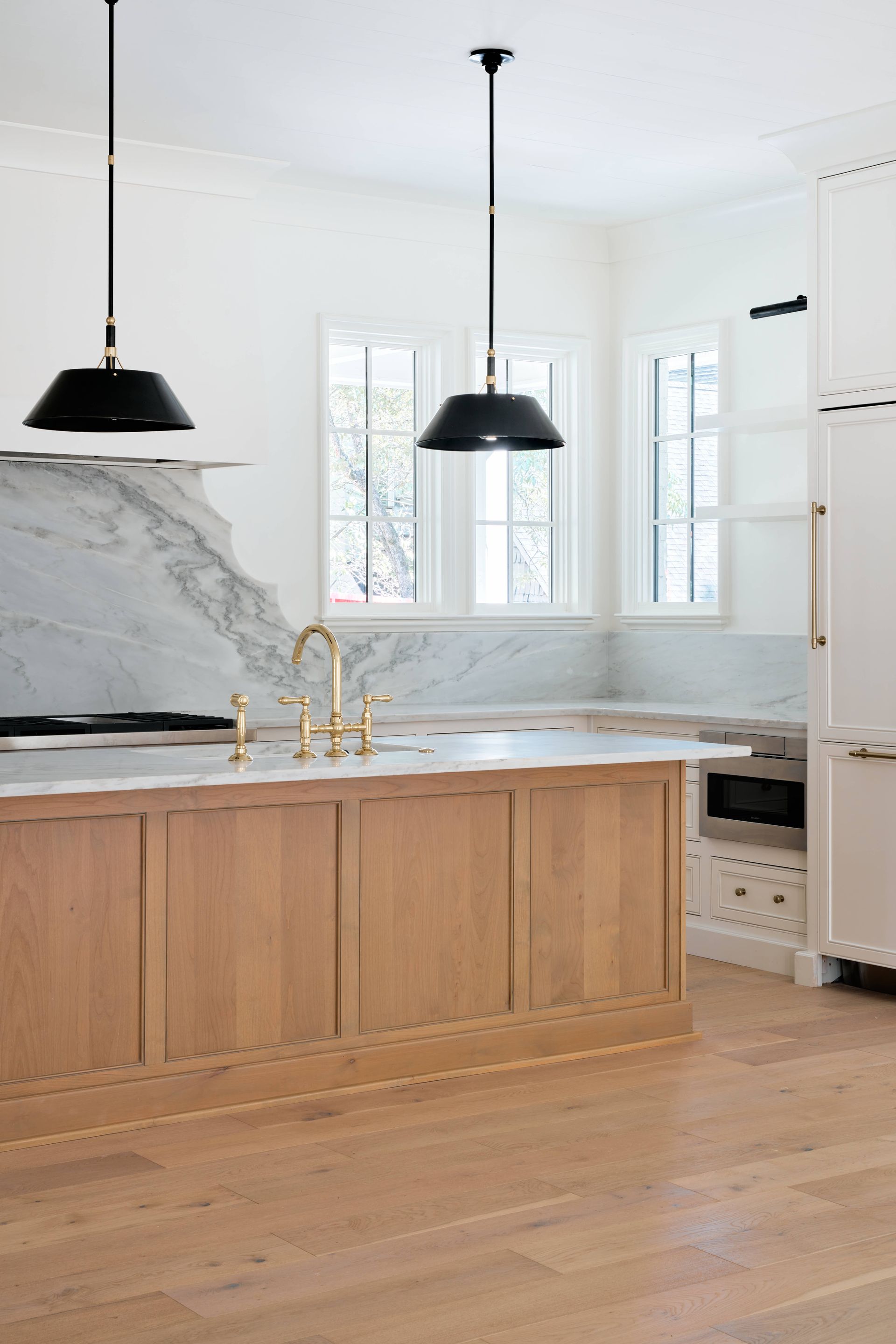 Bright modern kitchen with wood island, marble backsplash, black pendant lights, and white cabinets