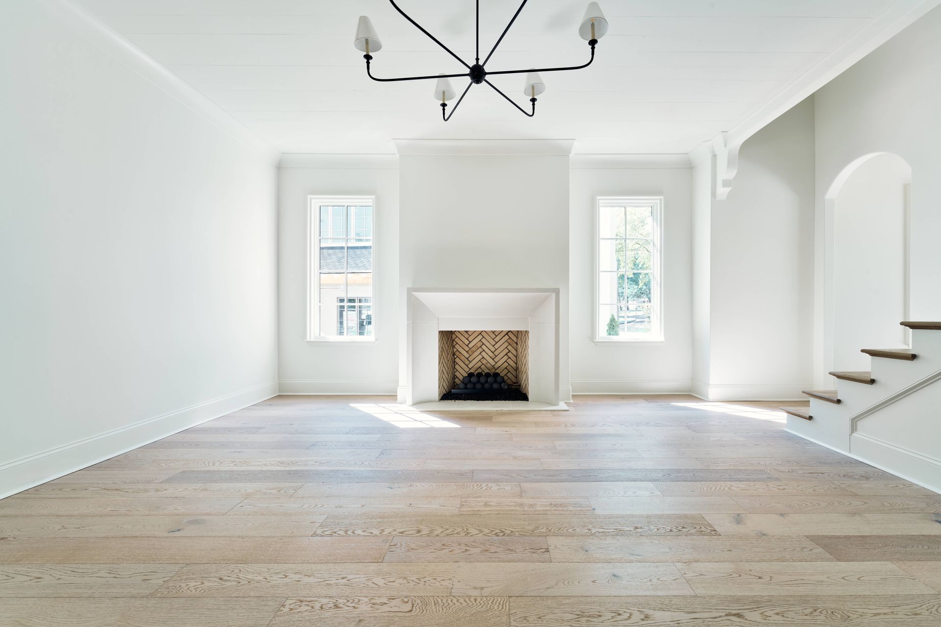 Bright empty living room with white walls, fireplace, hardwood floors, and stairs on the right.