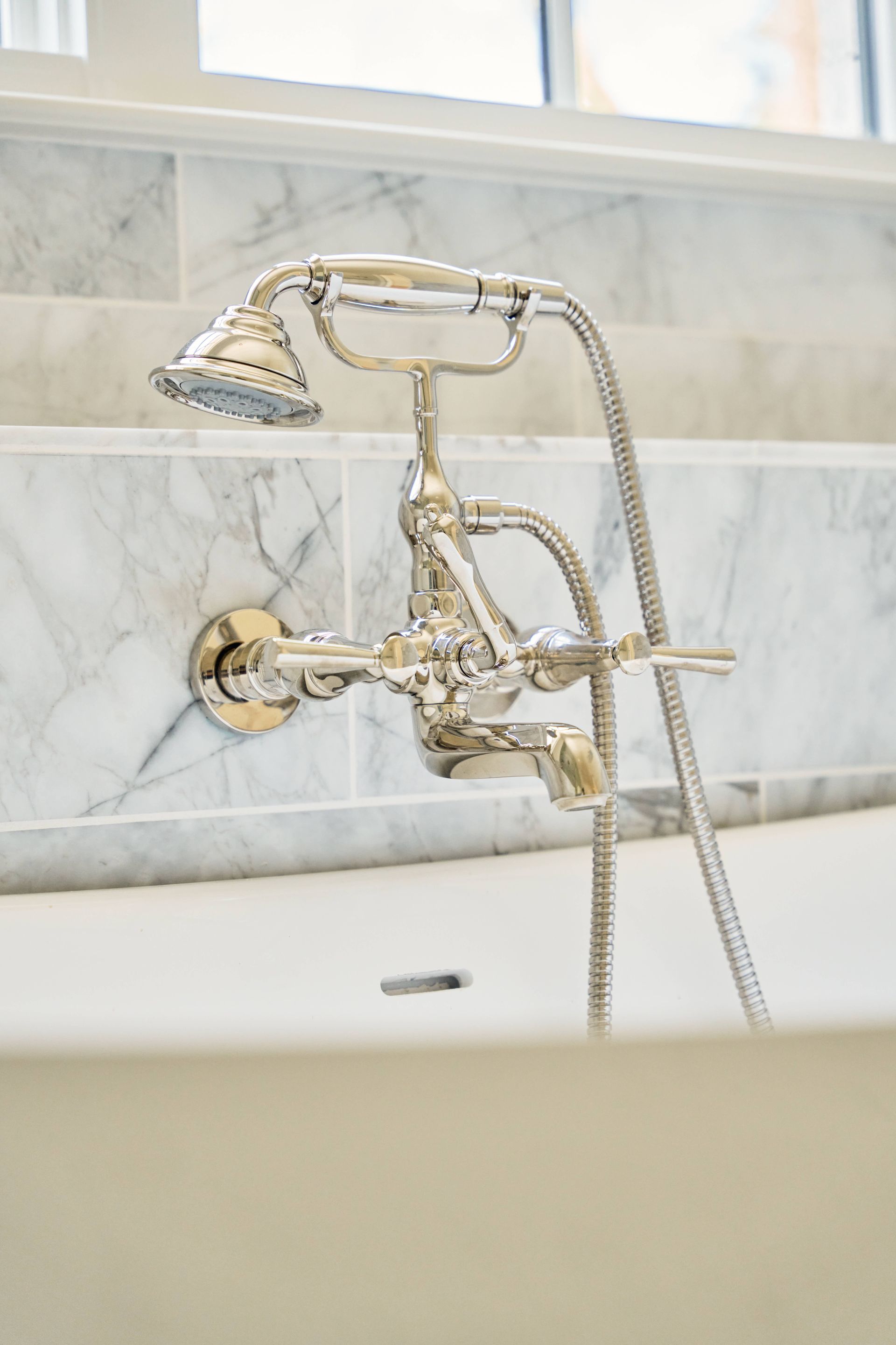 Chrome bathtub faucet with handheld shower head on a marble wall.