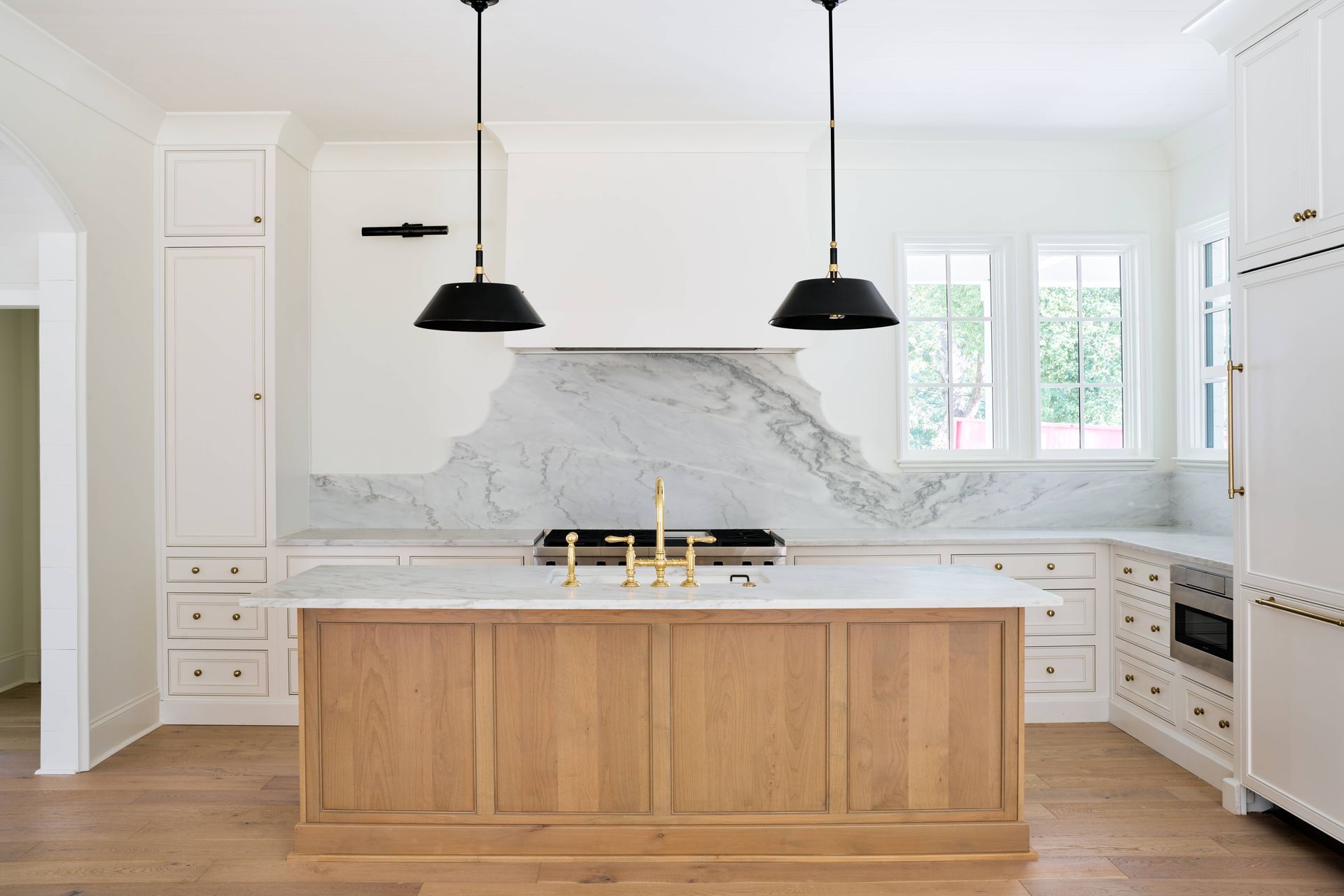 Bright modern kitchen with white cabinets, marble backsplash, wood island, and black pendant lights