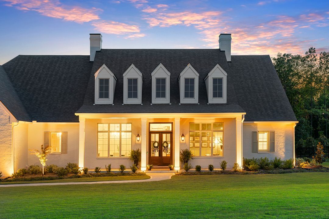 Well-lit suburban house at dusk with a dark roof, white trim, and warm lights glowing inside
