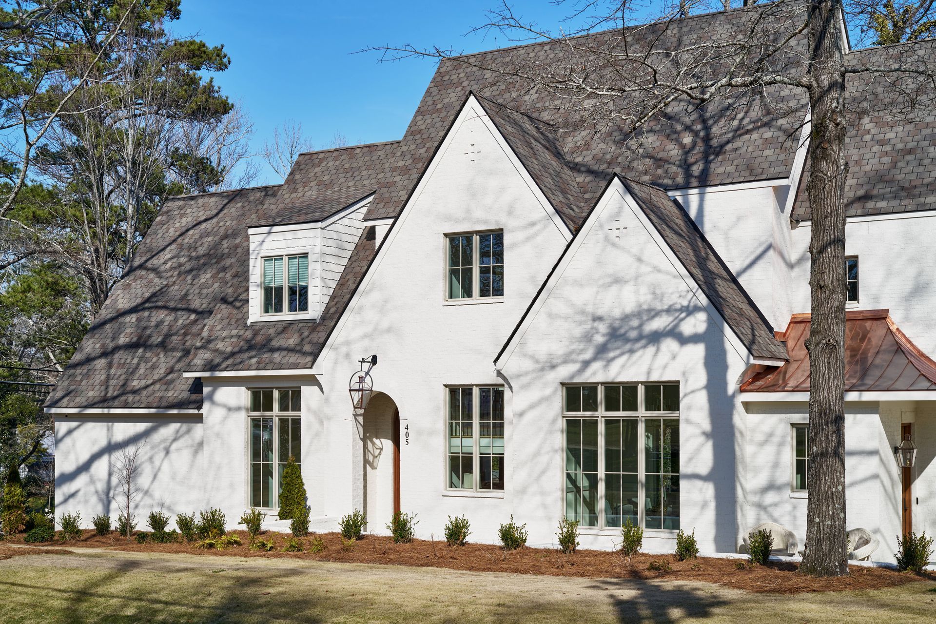 White two-story house with steep roof, tall windows, and a front lawn under a clear blue sky