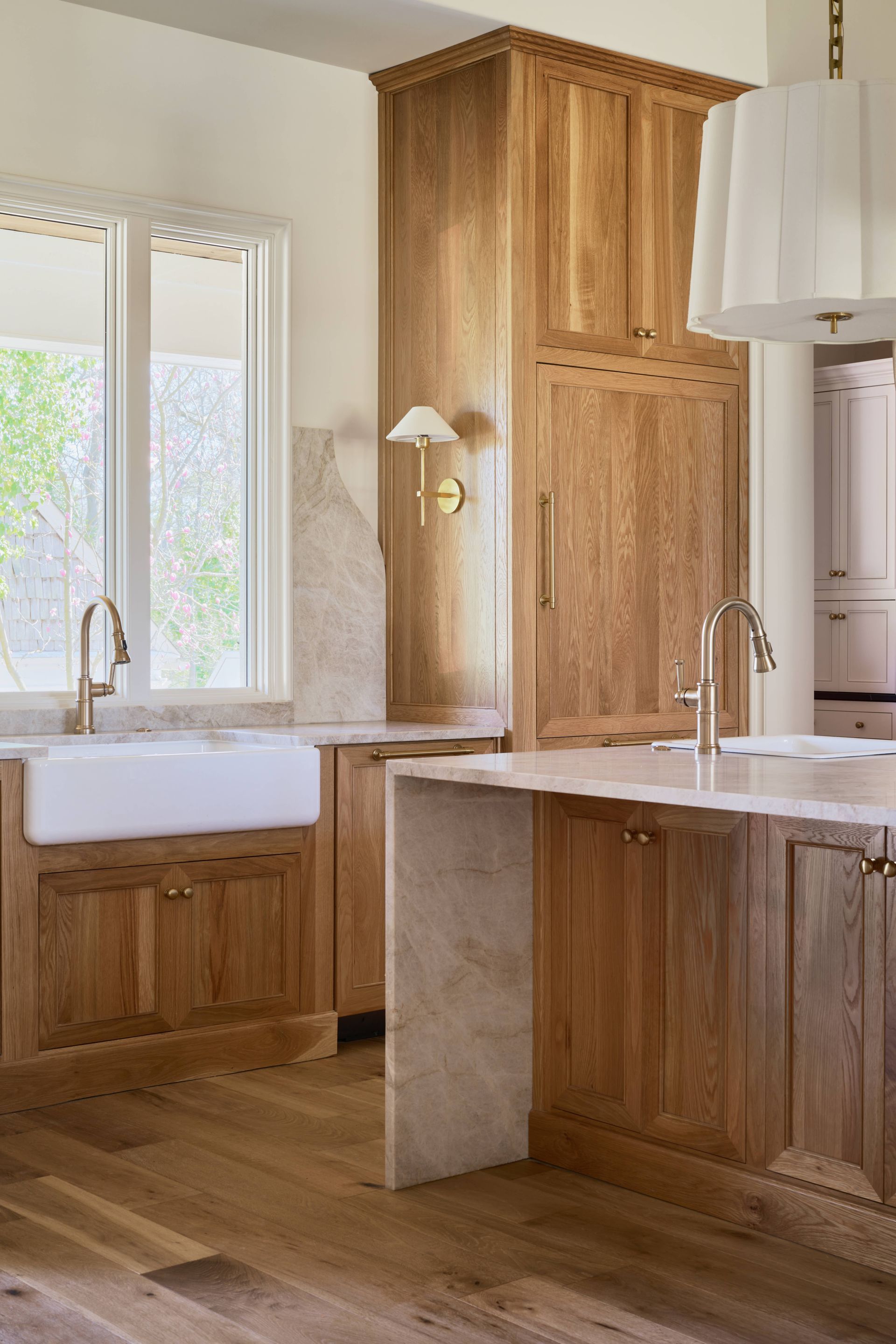 Warm wood bathroom with double sinks, marble vanity, and large mirrors in natural light