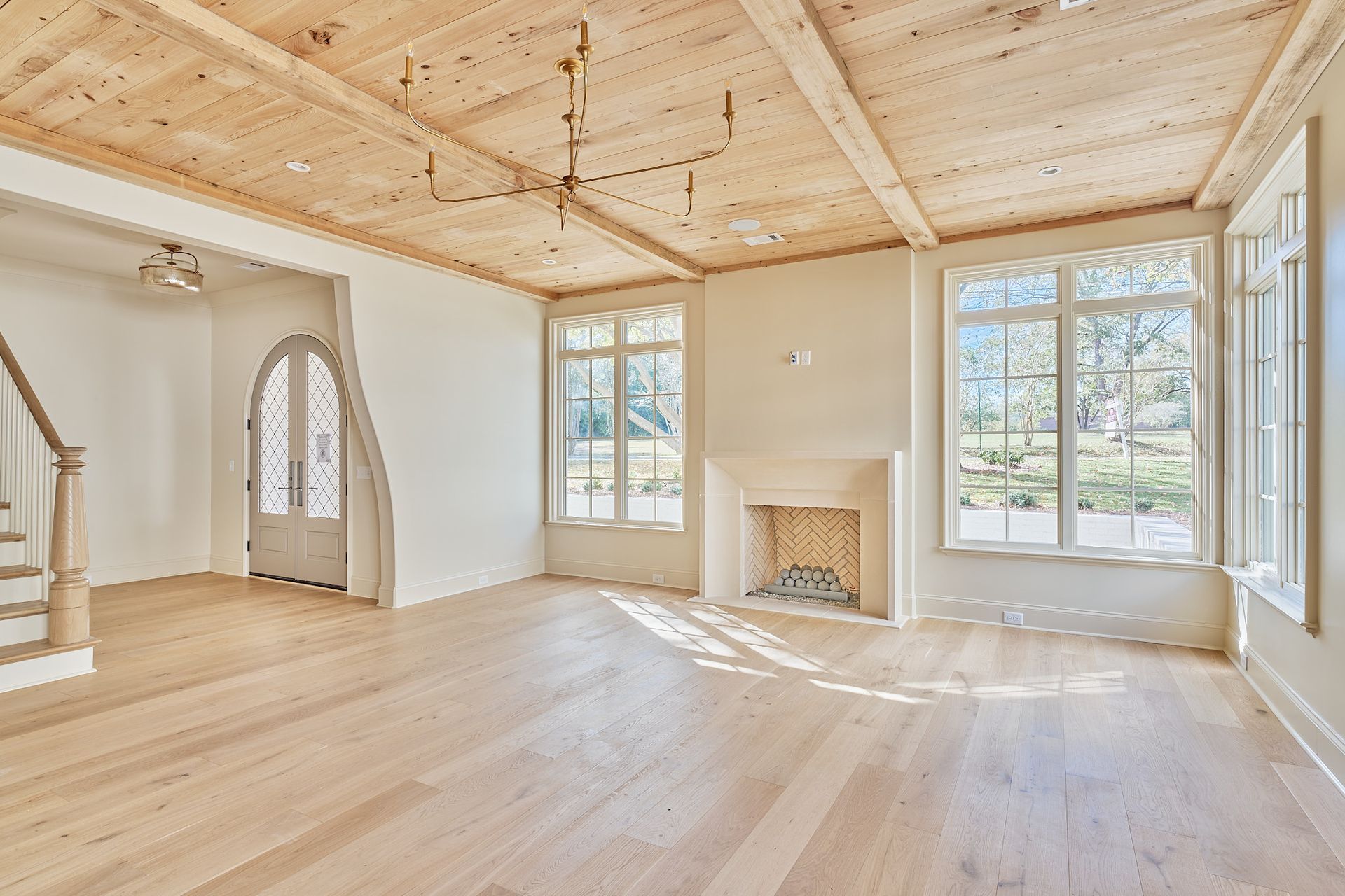 Bright empty living room with wood floors, exposed beam ceiling, fireplace, and large windows