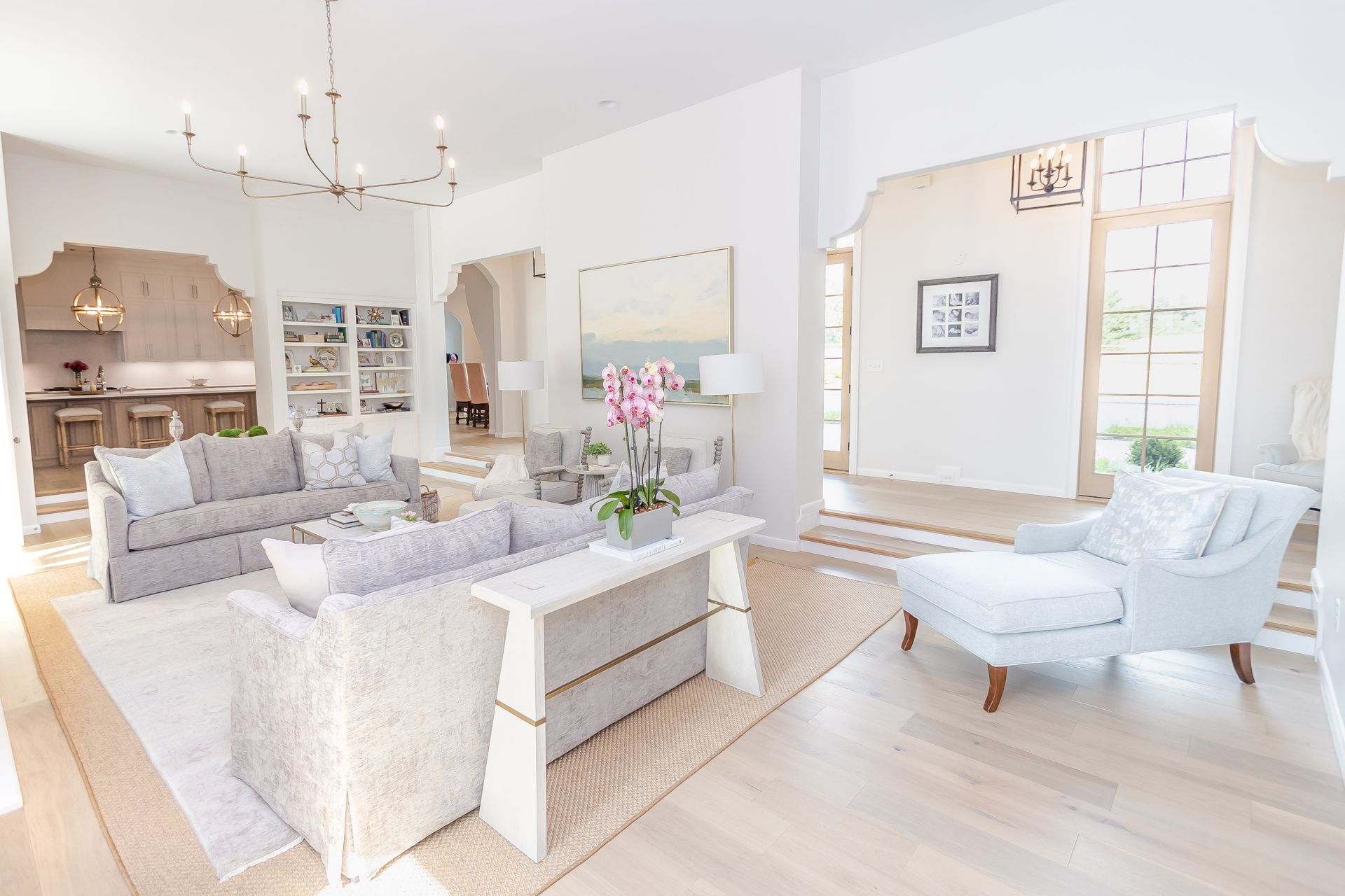 Bright modern living room with white sofas, a coffee table, and large windows overlooking a bright space