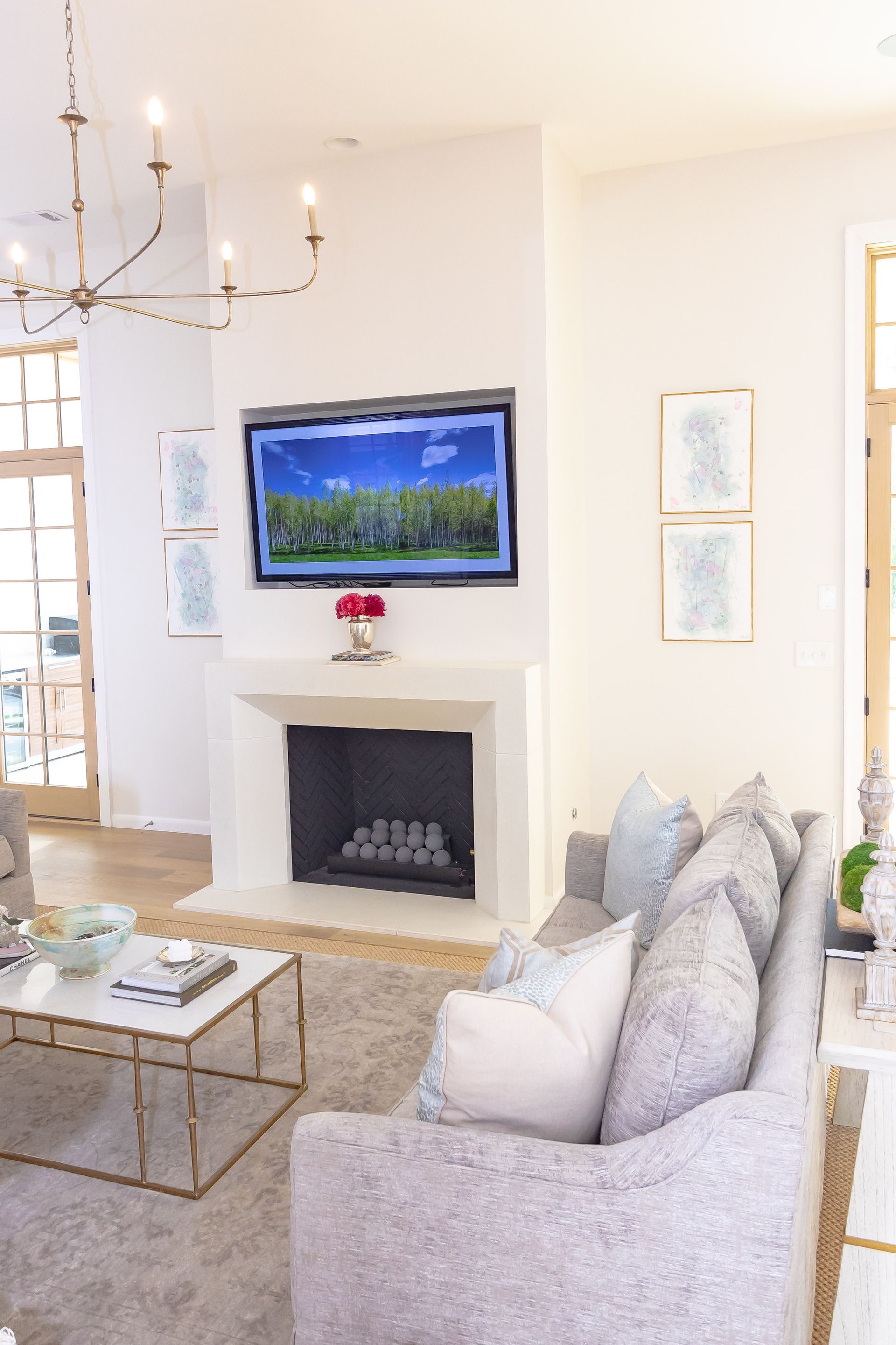 Bright living room with fireplace, wall-mounted TV, chandelier, and light gray sofa.