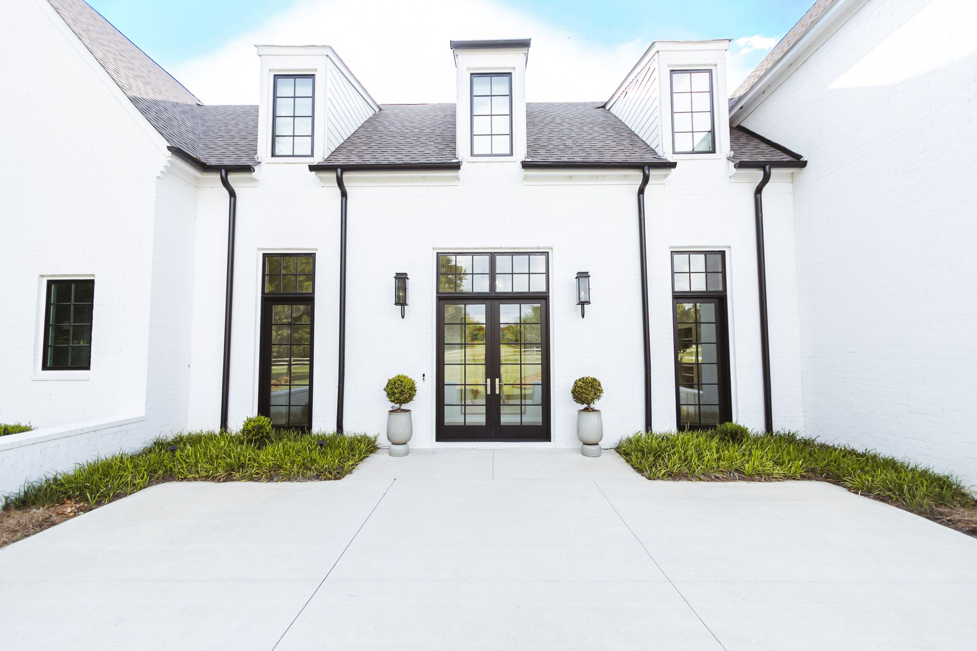 Modern white house facade with black-framed windows, double doors, and landscaped entryway