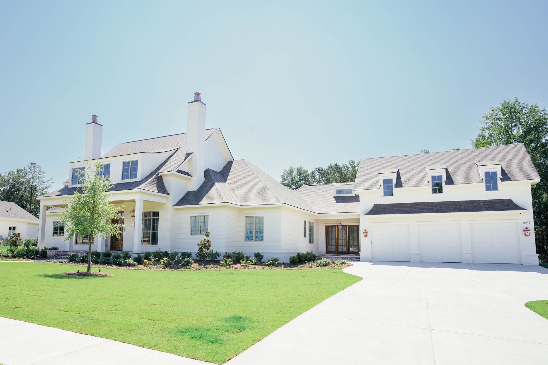 Large white suburban house with a two-car garage, green lawn, and bright driveway under a clear sky