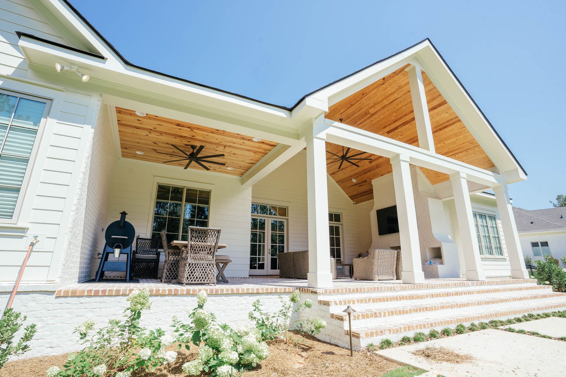 Modern farmhouse porch with white columns, wood ceilings, and outdoor seating in bright sunlight