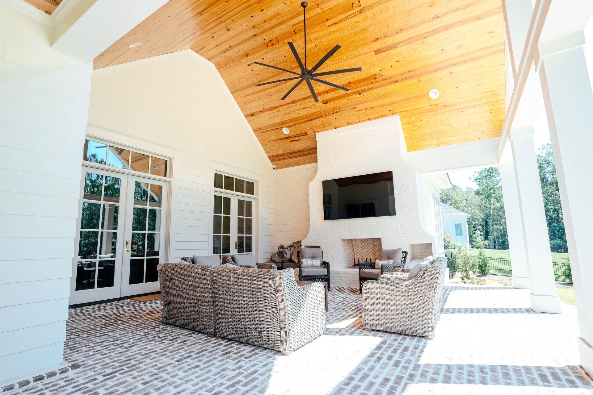 Bright covered patio with wicker seating, patterned tile floor, and a wood ceiling with black ceiling fan.