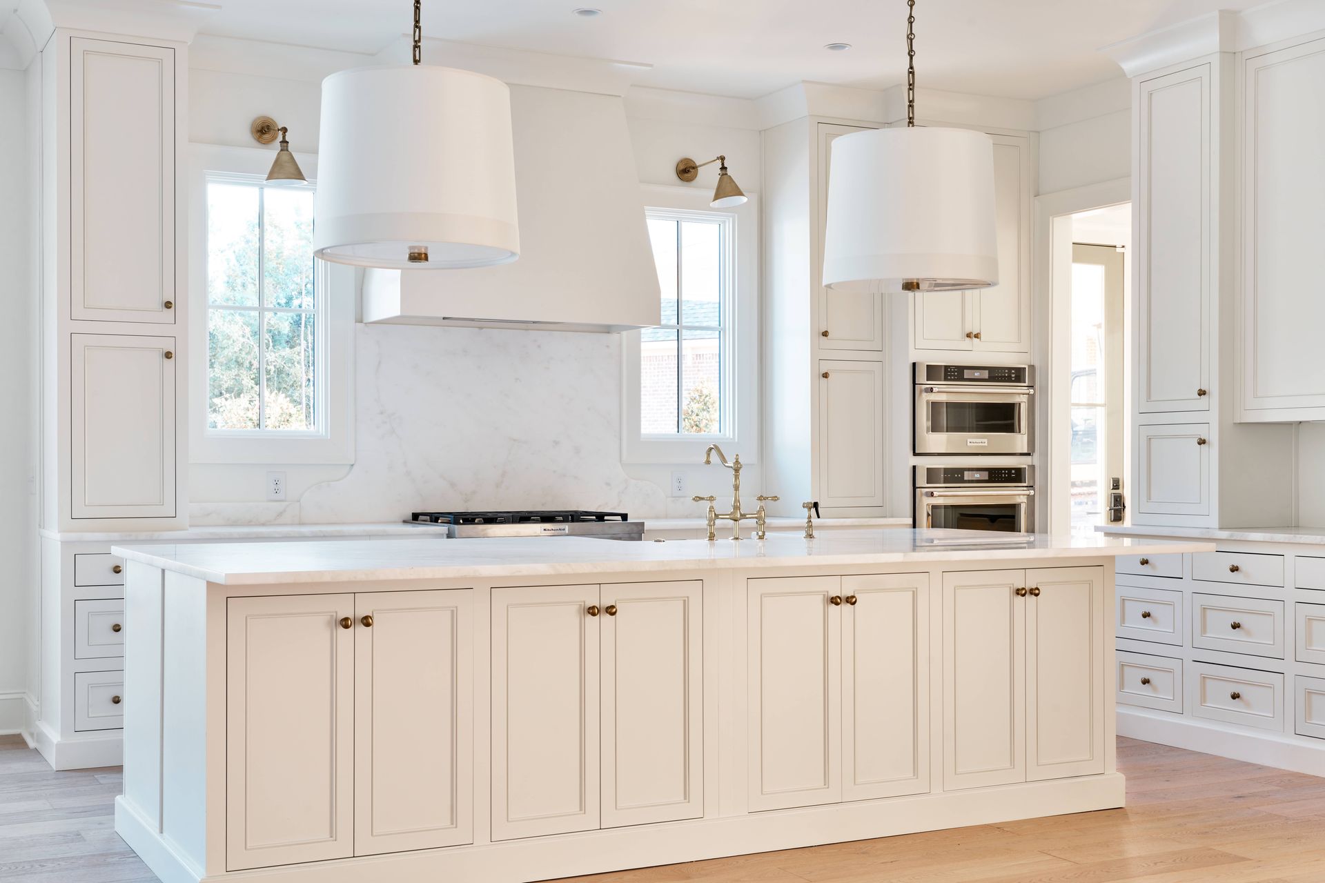 Bright white modern kitchen with large island, pendant lights, and built-in oven.
