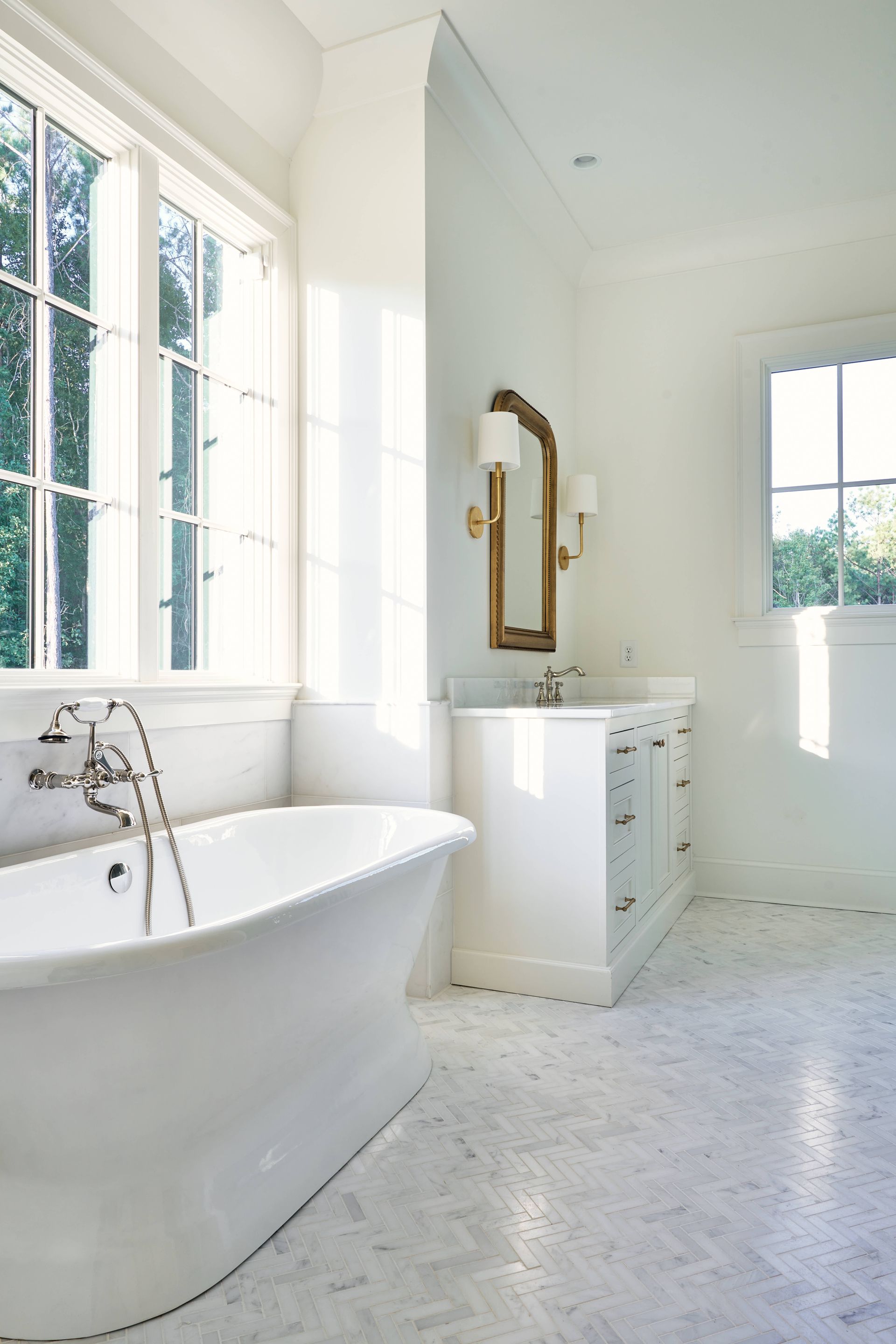 Bright white bathroom with freestanding tub, vanity, mirror, and large sunlit windows