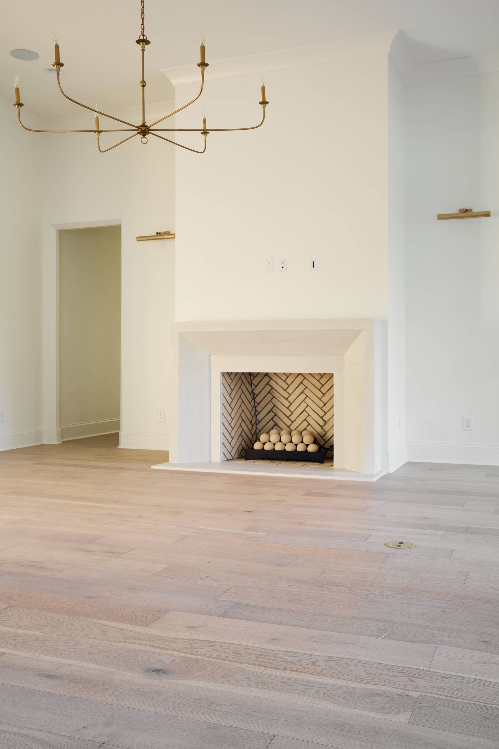 Empty white room with a fireplace, brass chandelier, and light wood floors