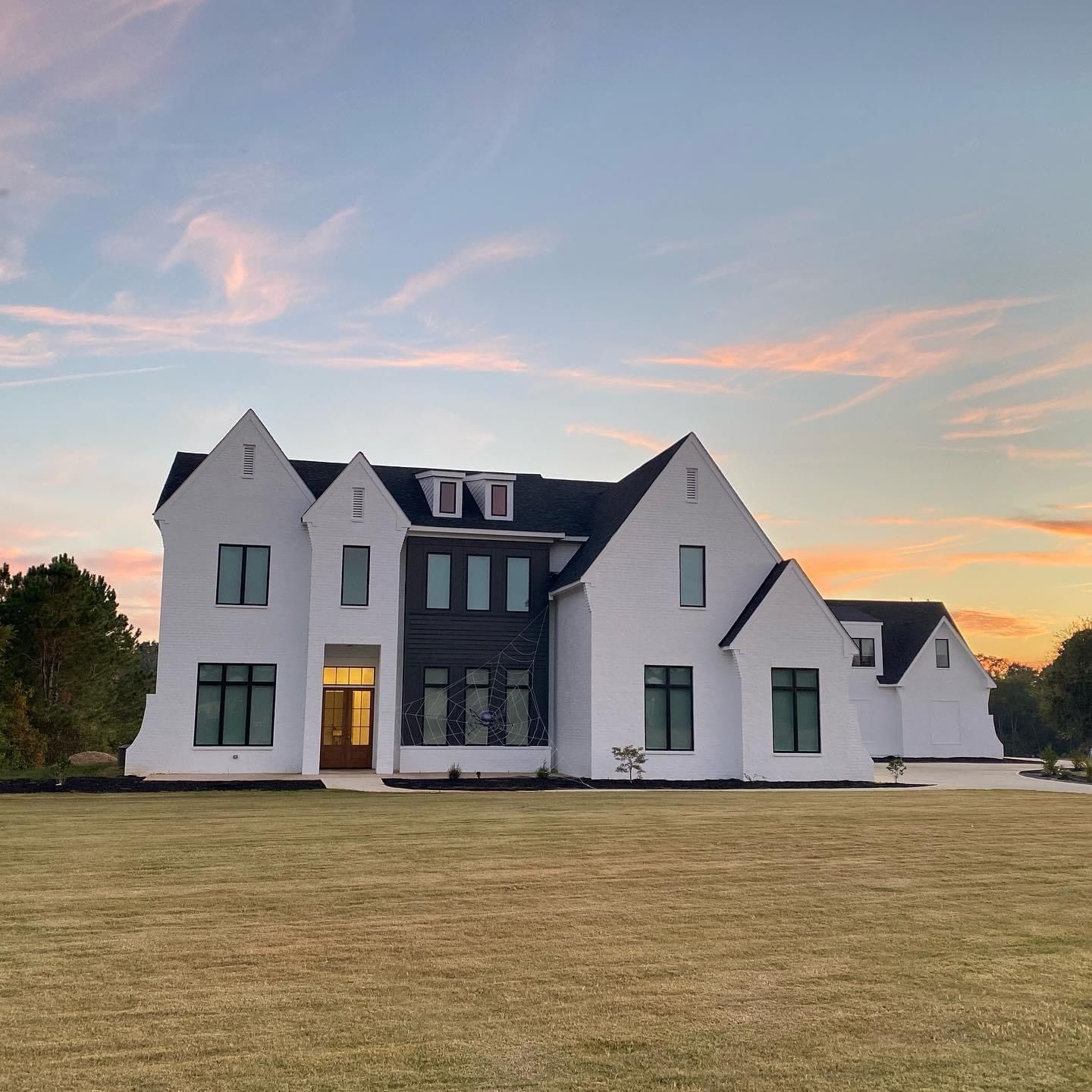 Large white house with dark roof at dusk under a pastel sunset sky