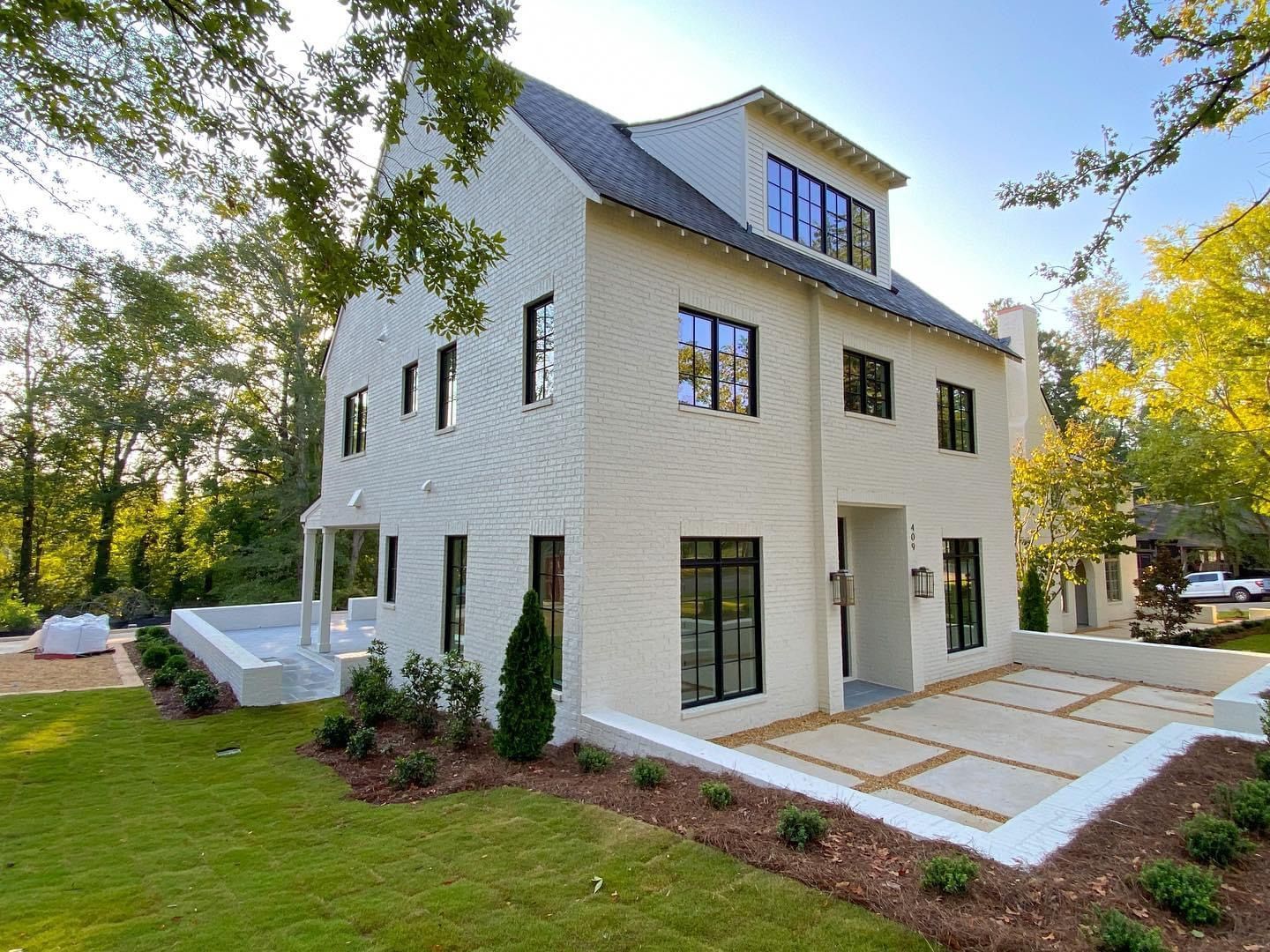 White two-story modern house with black windows, gray roof, and a landscaped yard