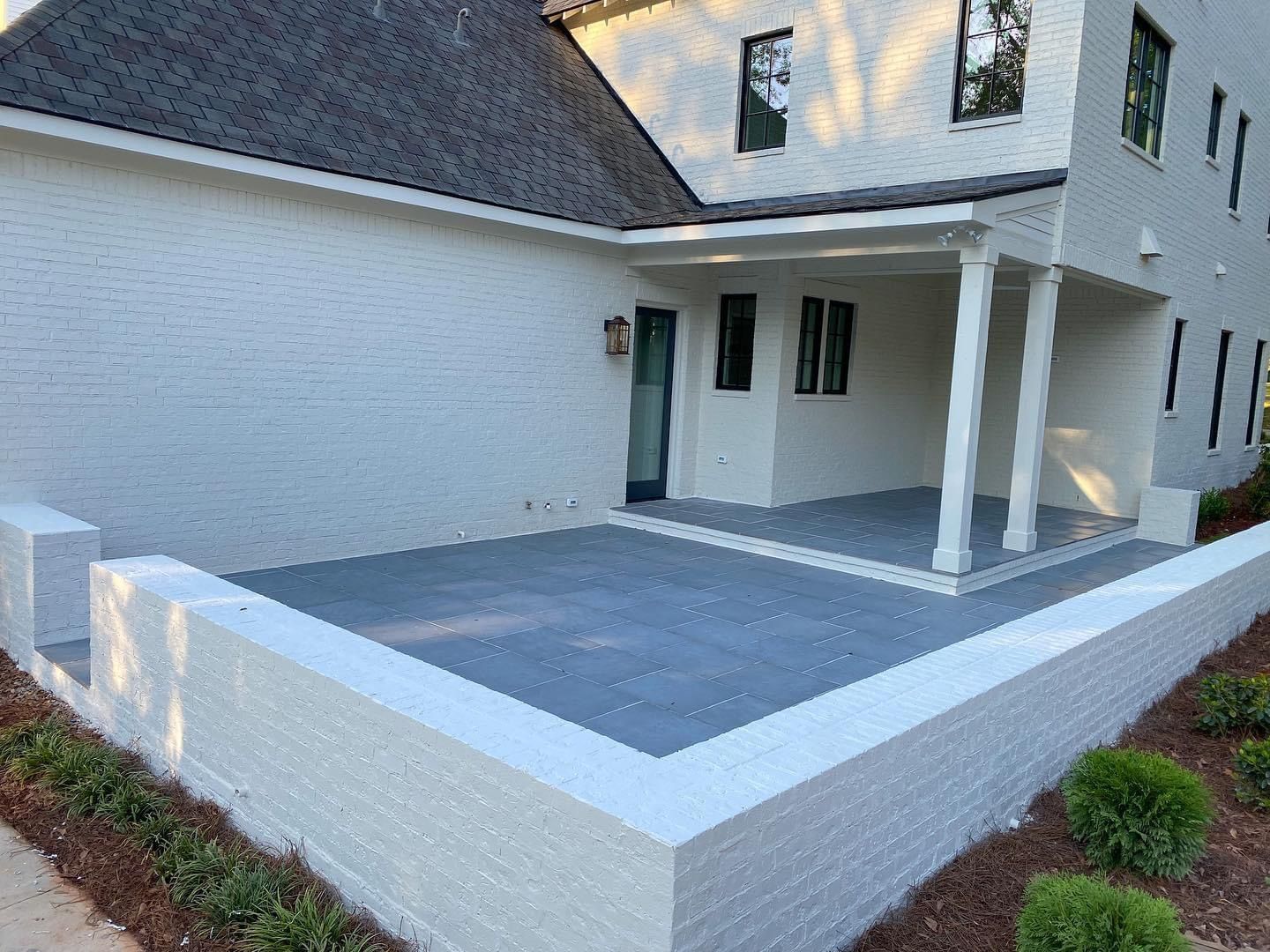 White modern house with a covered patio and low white wall surrounding a gray paved courtyard.