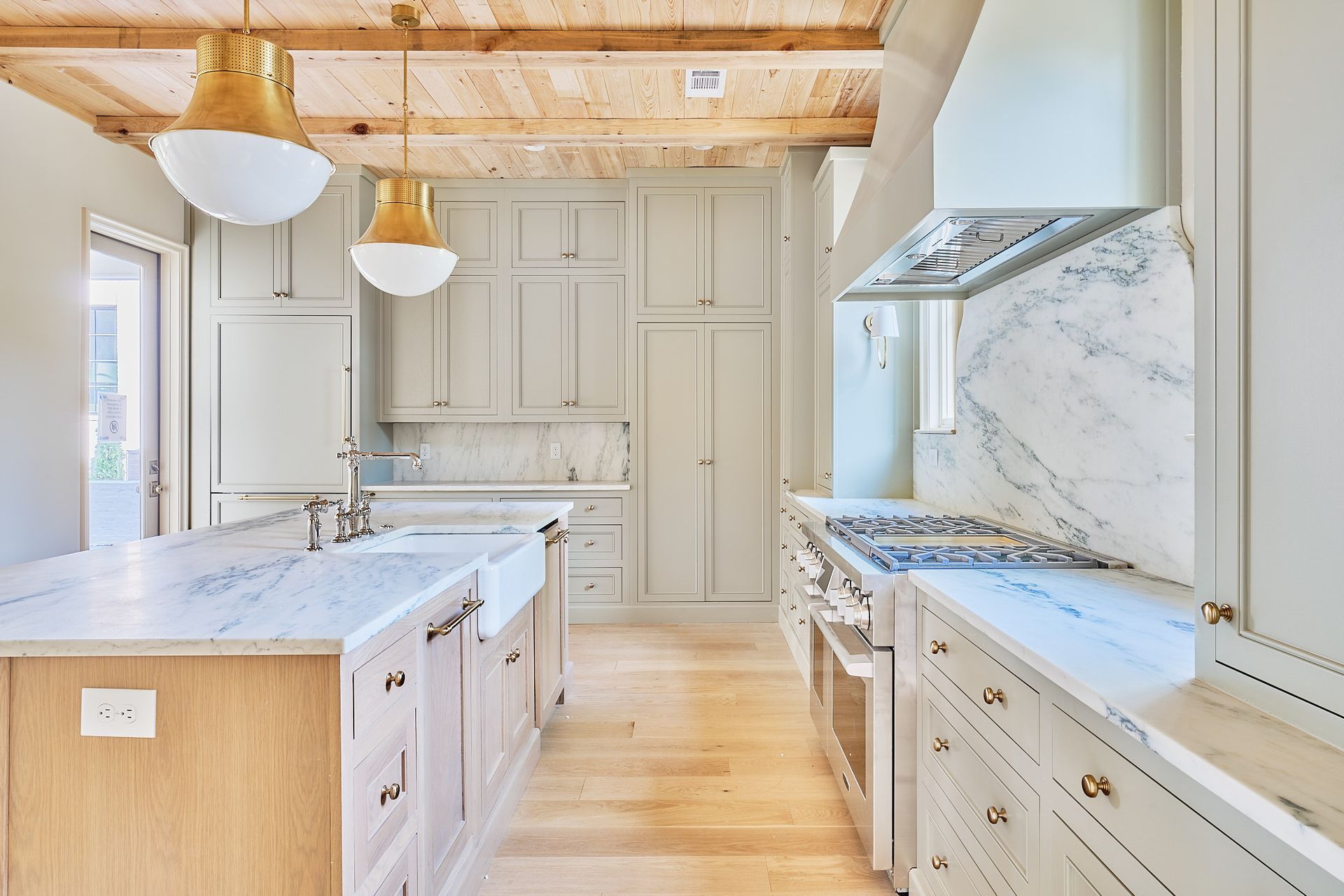 Bright modern kitchen with white cabinets, marble island, wood ceiling, and pendant lights