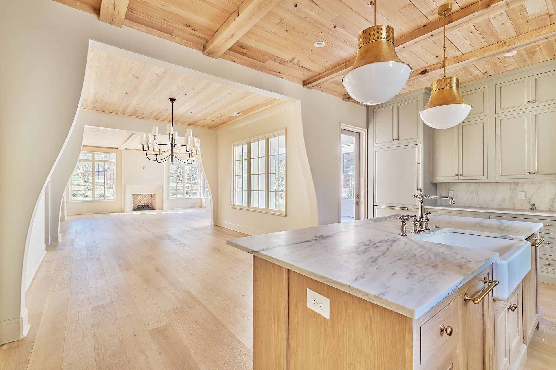 Bright open kitchen with white cabinetry, wood beams, and light hardwood floors leading into a dining area