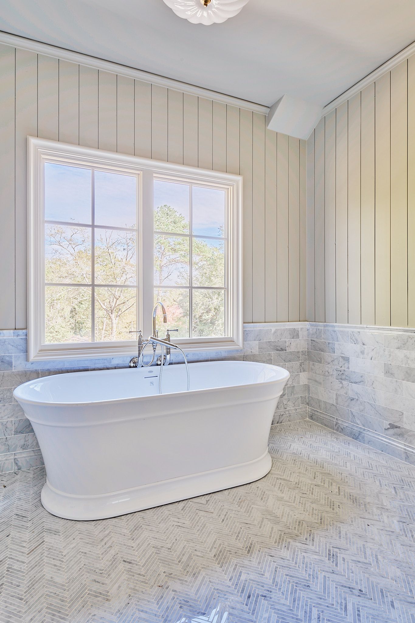 Bright bathroom with freestanding tub, marble-look surfaces, and large window overlooking trees