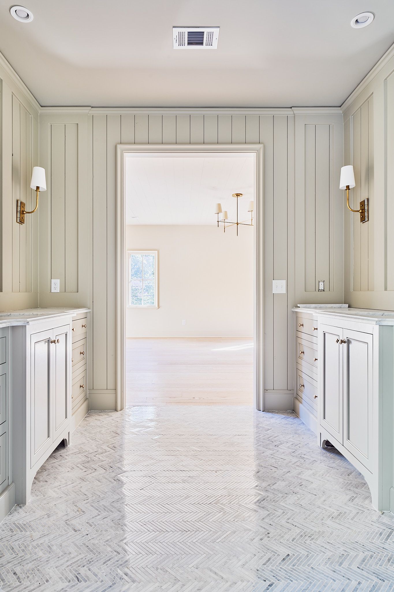 Bright narrow hallway with white paneled walls, patterned runner, and open doorway to a sunlit room