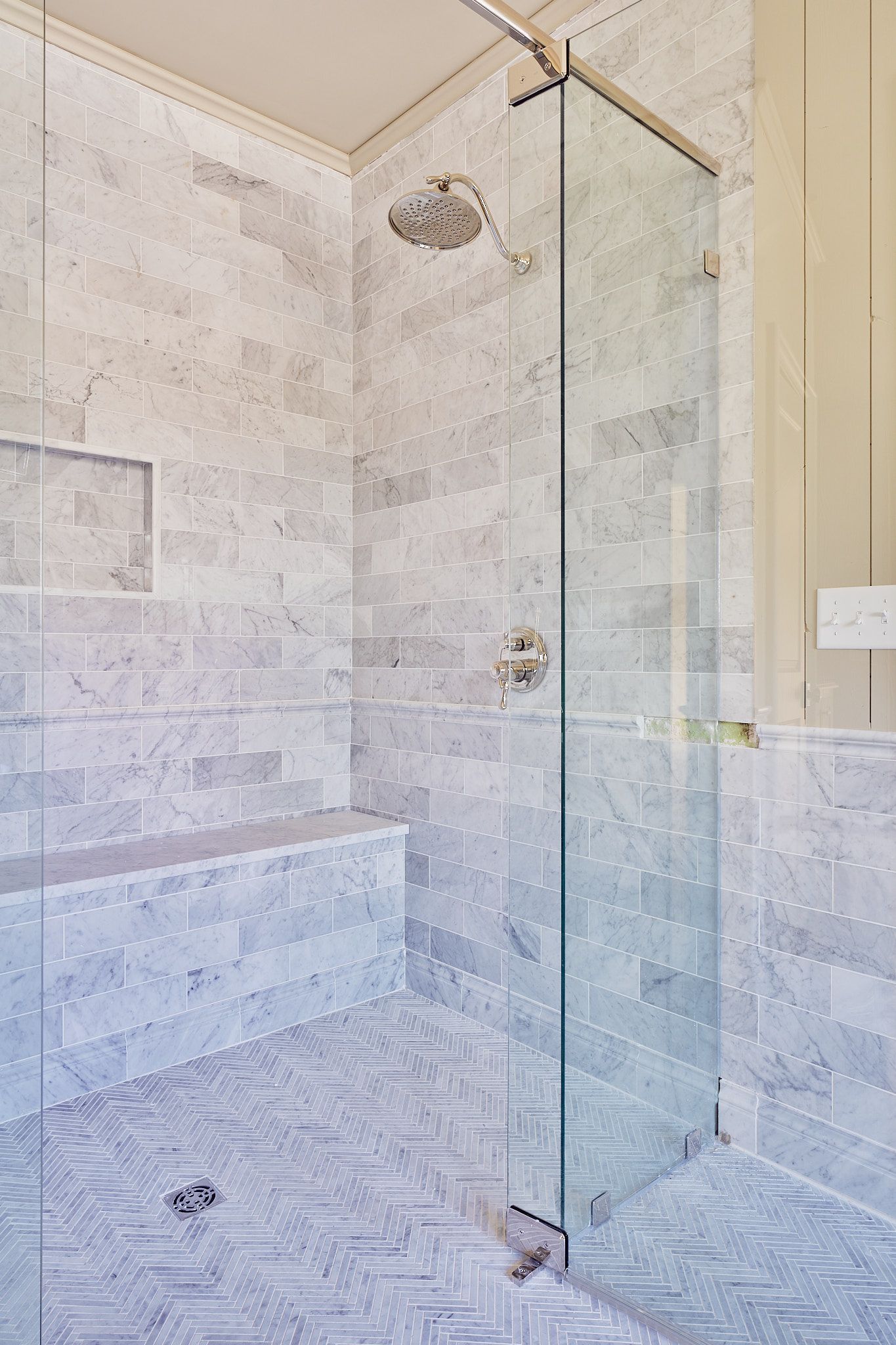 Glass-enclosed shower with light stone tile, built-in bench, and chrome fixtures