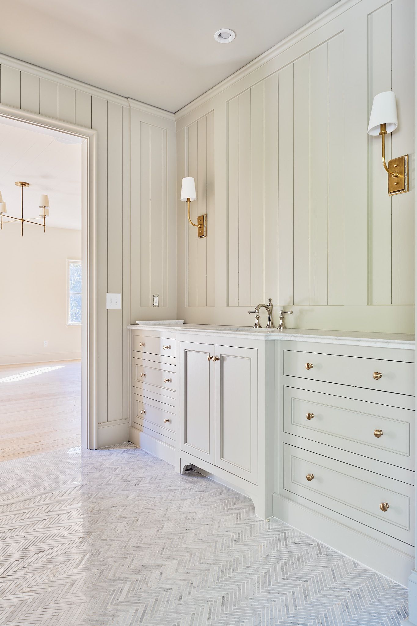 Elegant white bathroom with marble floor, paneled walls, vanity cabinets, and gold sconces