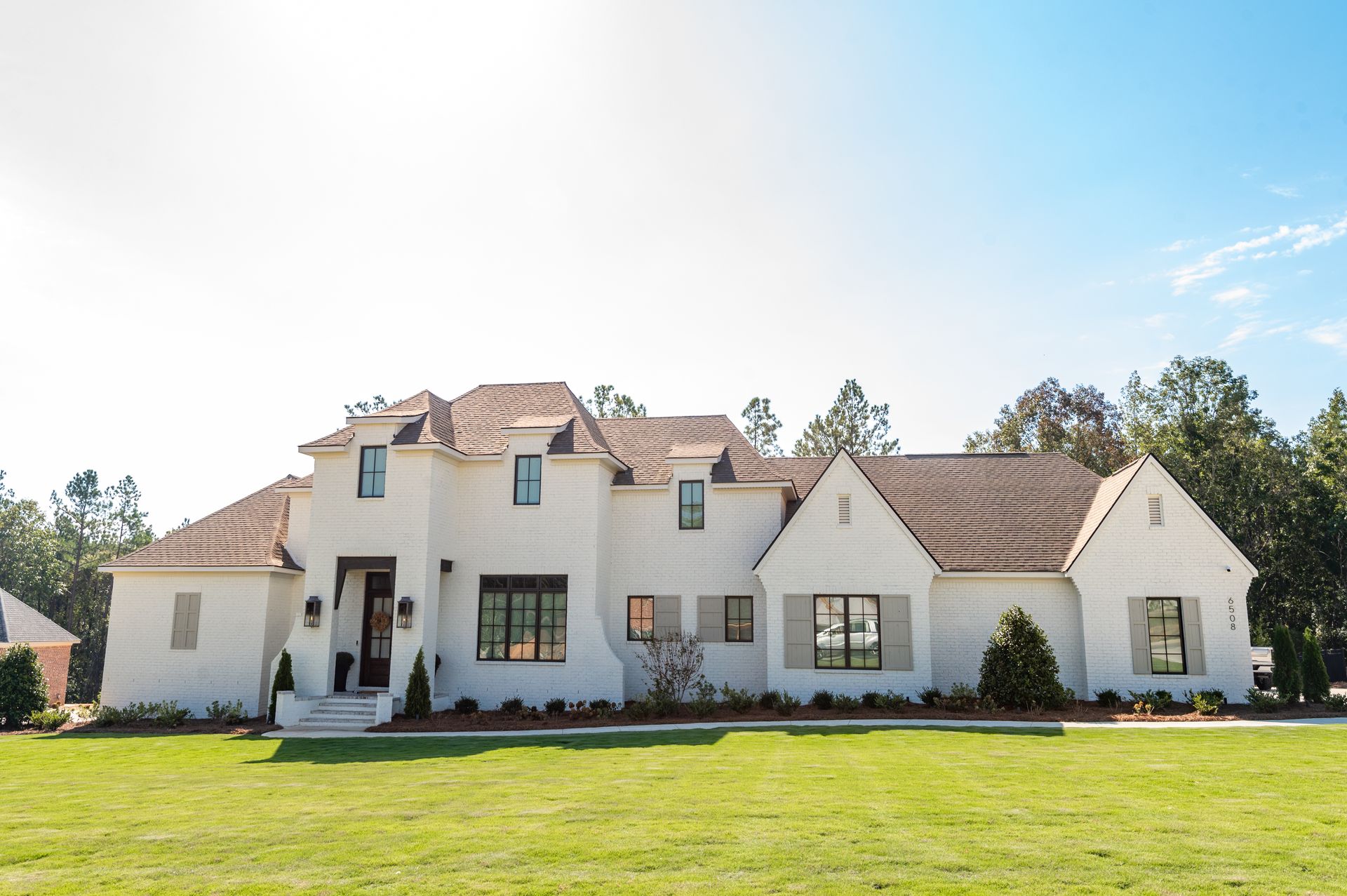 Large white suburban house with tan roof and manicured lawn under a bright blue sky