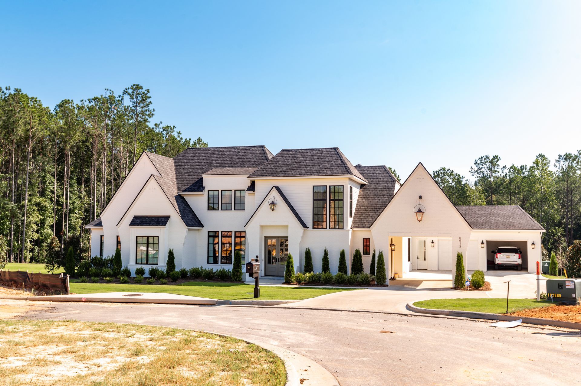 Large white suburban house with a dark roof, front lawn, and curved driveway under a blue sky