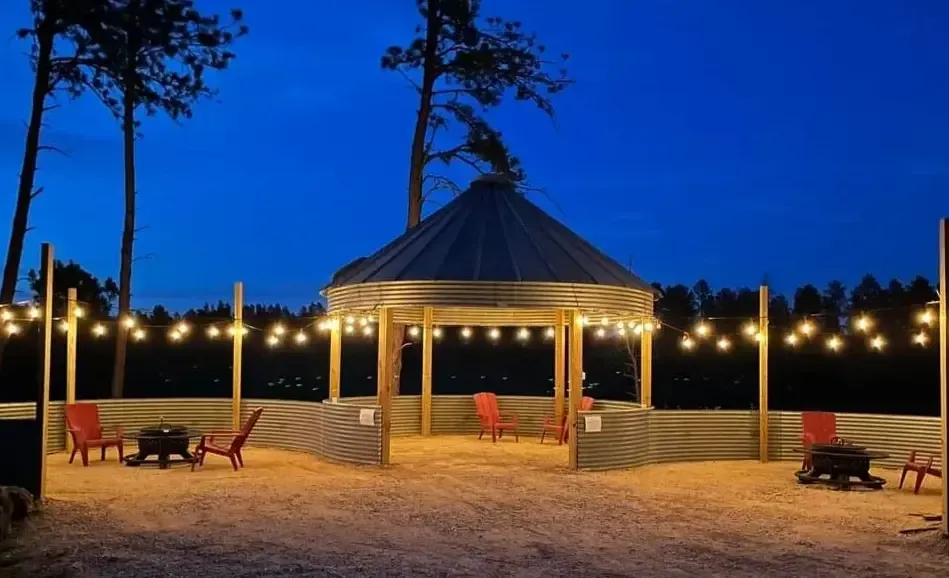 a gazebo with a fire pit and chairs is lit up at night .