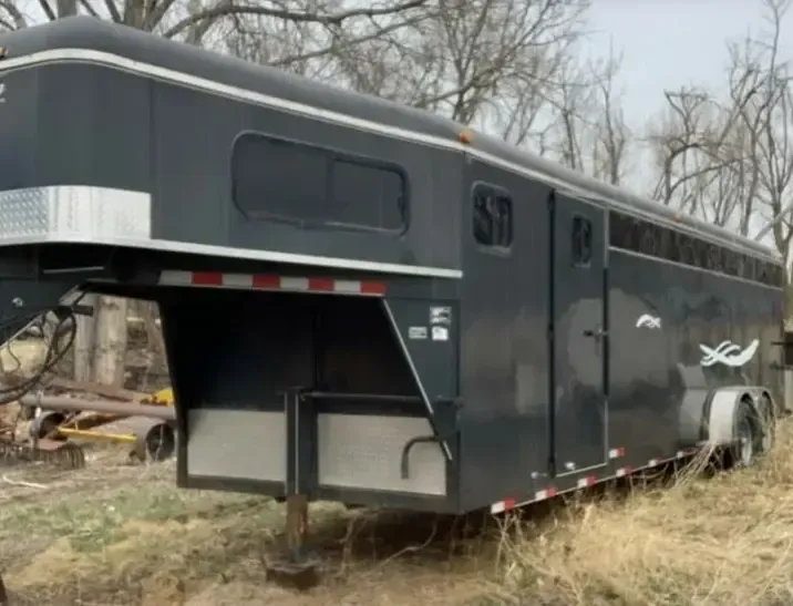 a black horse trailer is parked in a field .